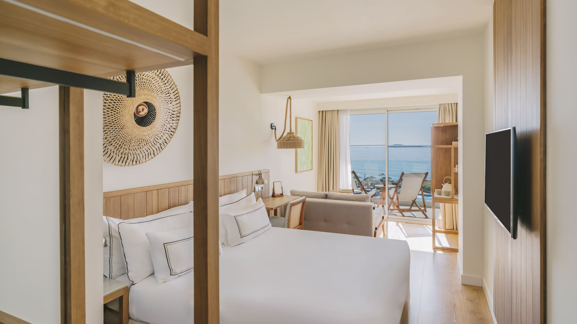 Modern hotel room with king bed, ocean view balcony, and wood decor.