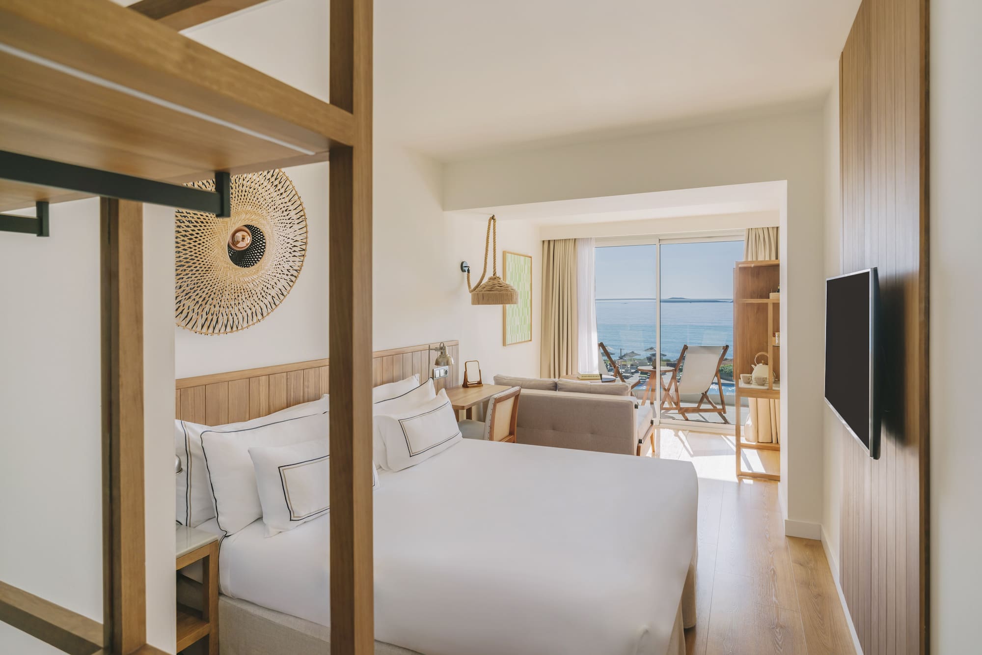 Modern hotel room with king bed, ocean view balcony, and wood decor.