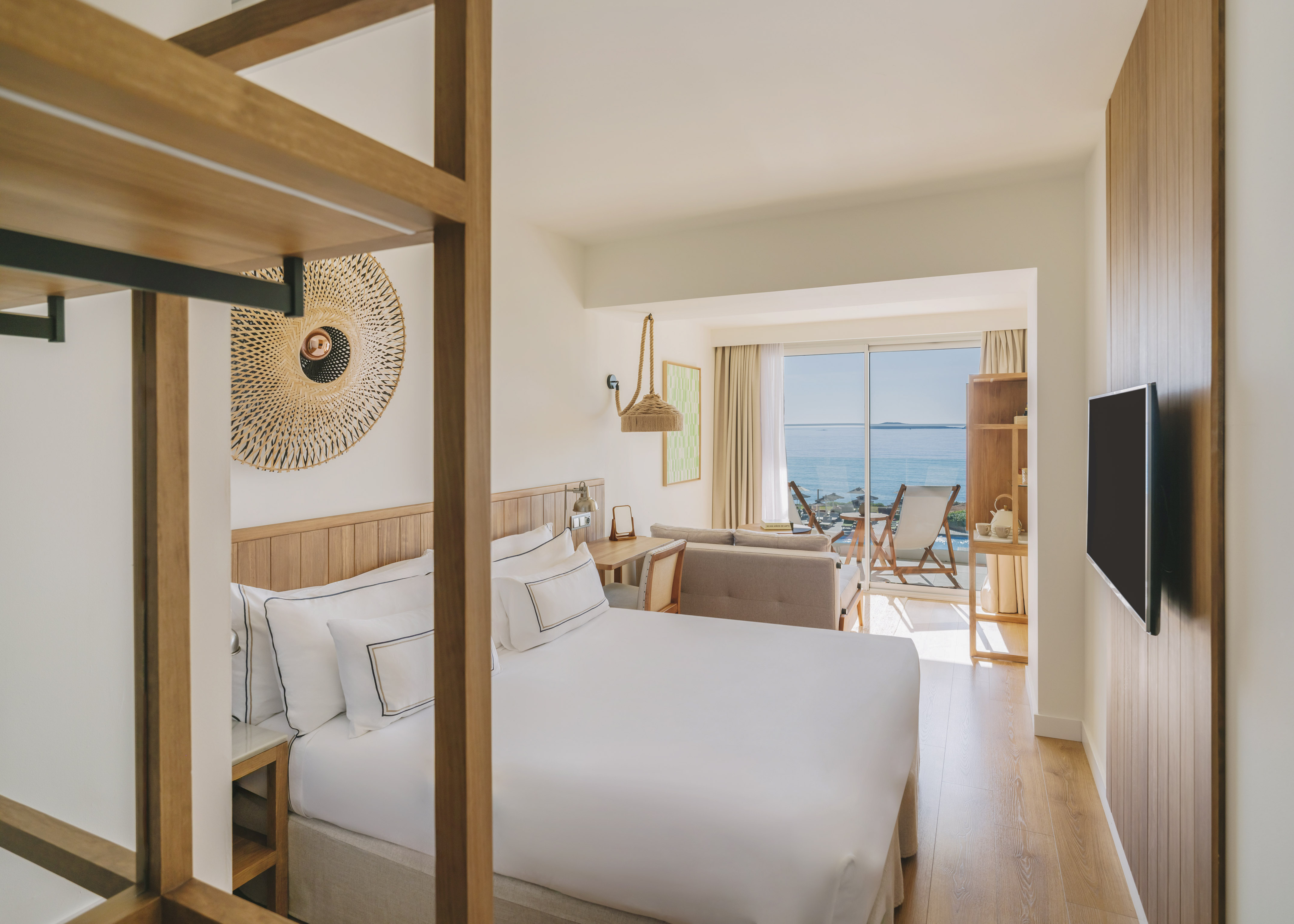 Modern hotel room with king bed, ocean view balcony, and wood decor.
