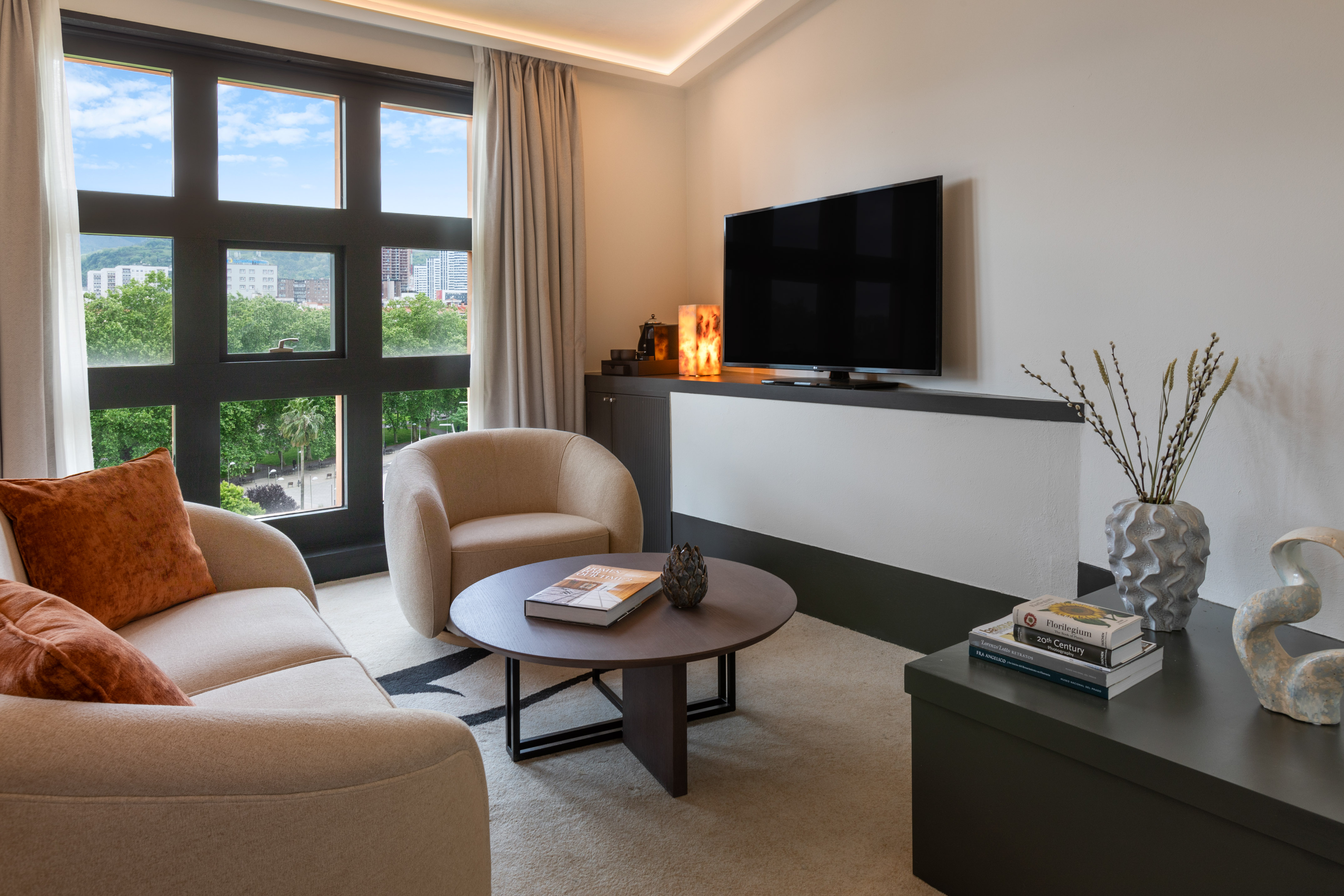 Modern hotel living room with city view, comfortable sofa, and TV.