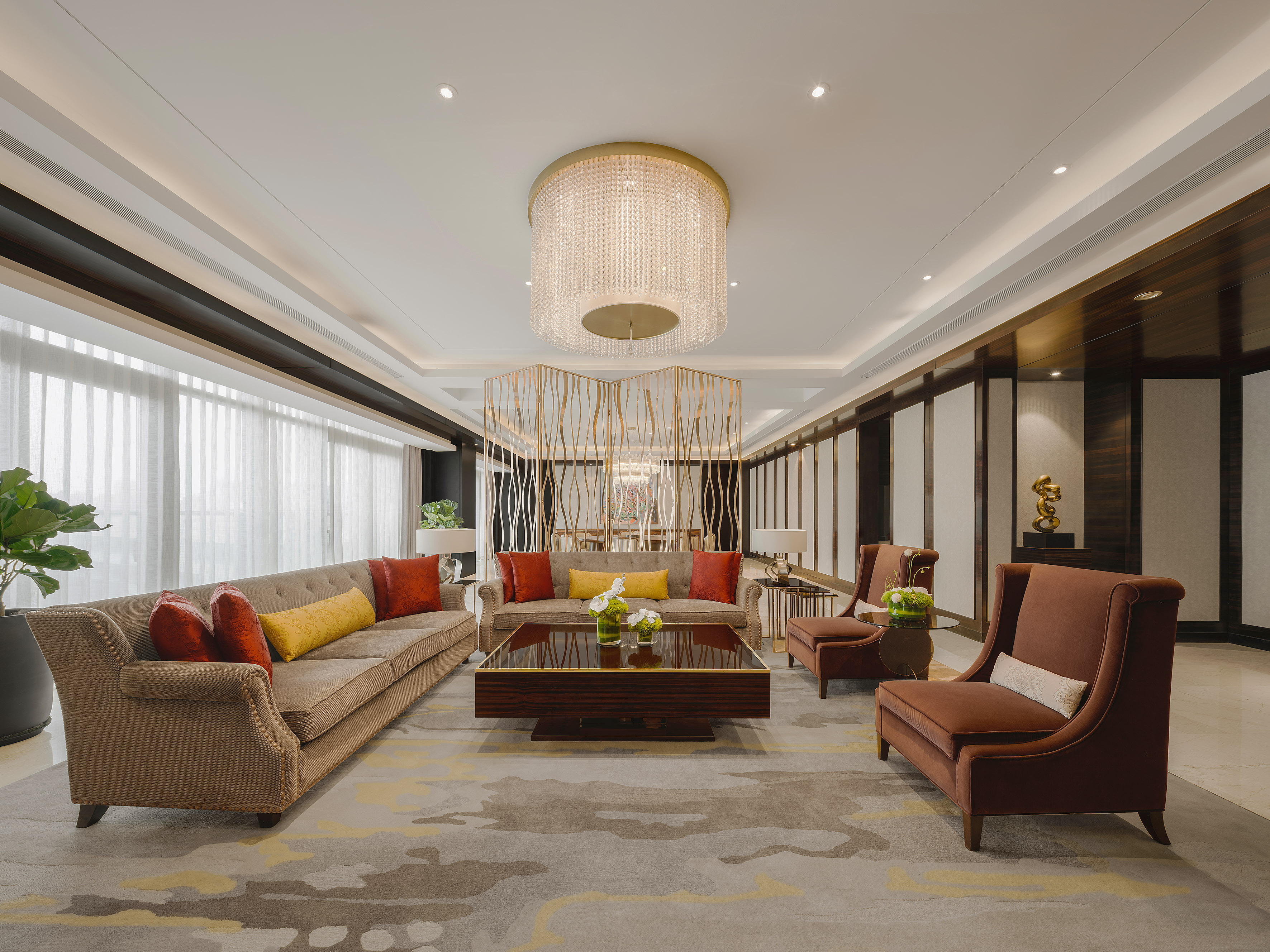 Luxury hotel lounge with modern sofa, brown armchairs, and crystal chandelier.