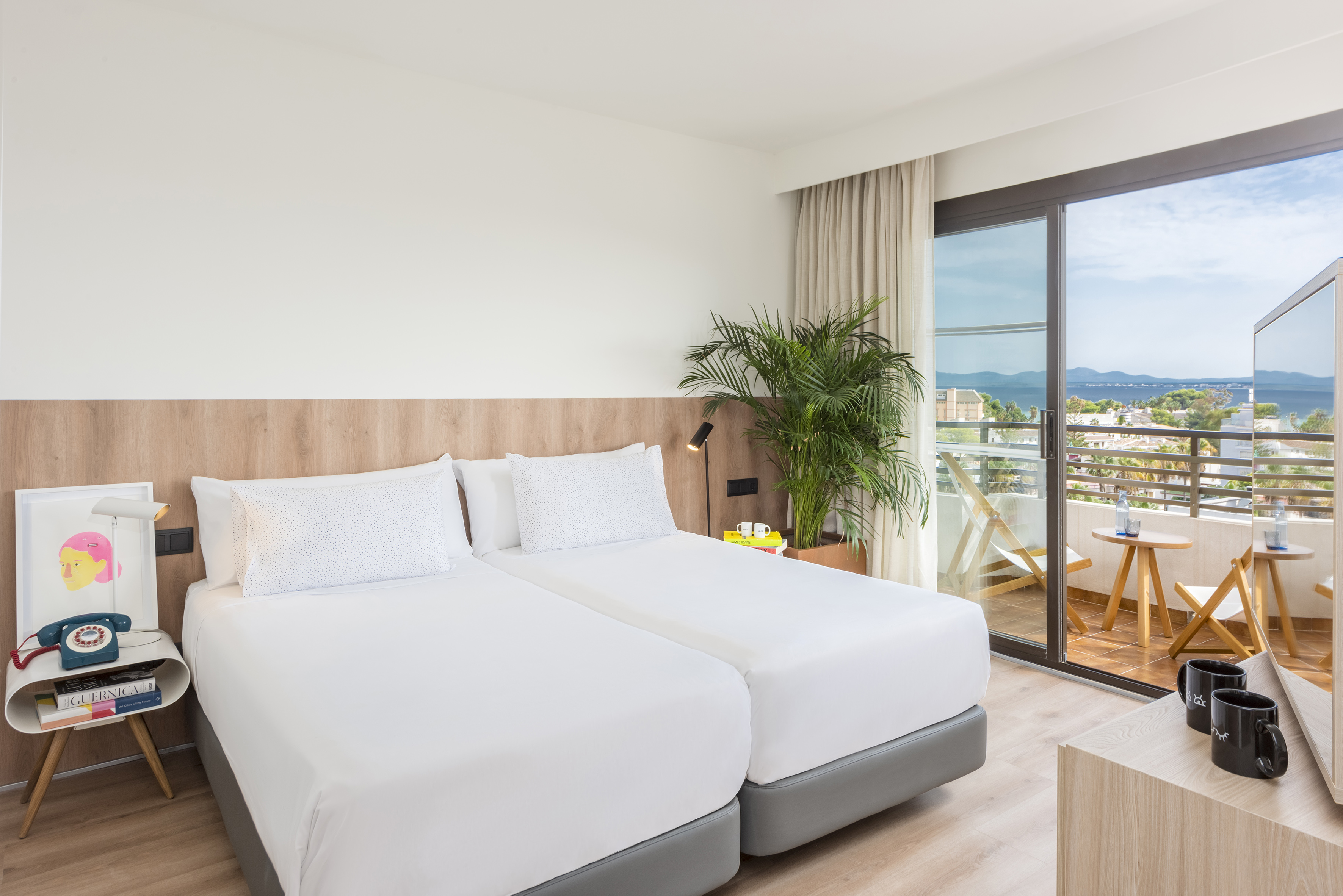 Modern hotel room with twin beds, wooden headboard, and balcony sea view.