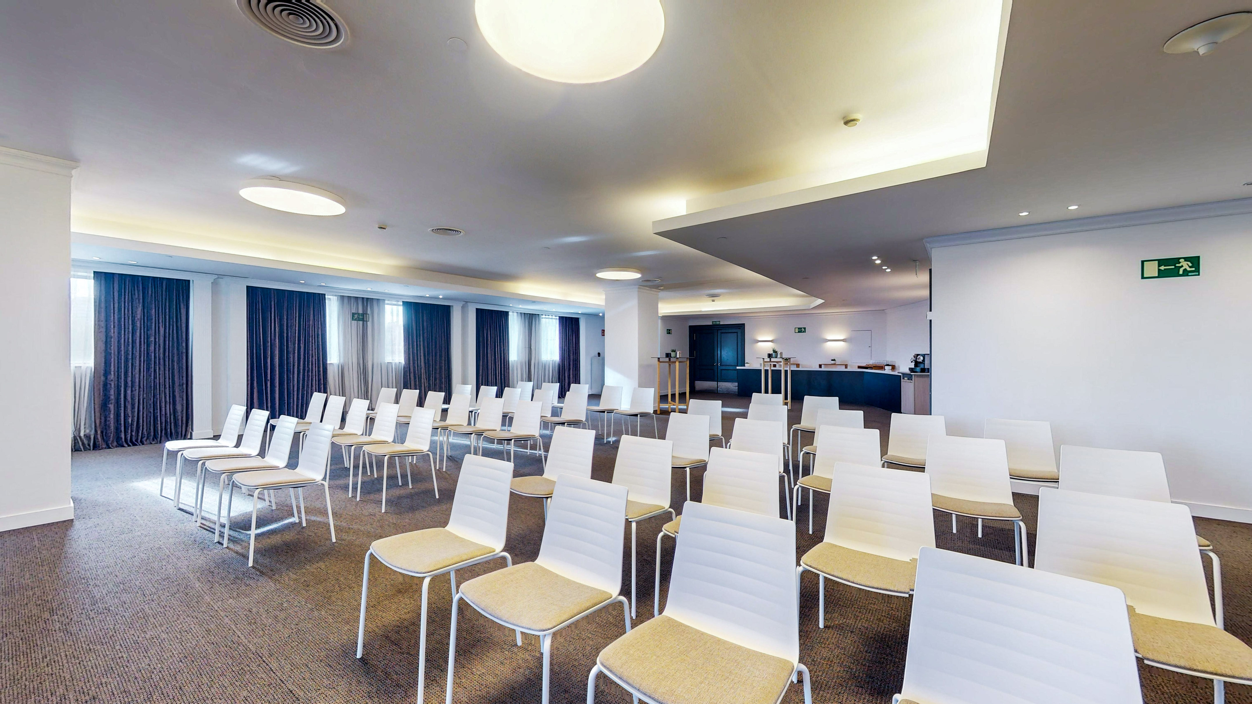Modern empty conference room with rows of white chairs and dark curtains.