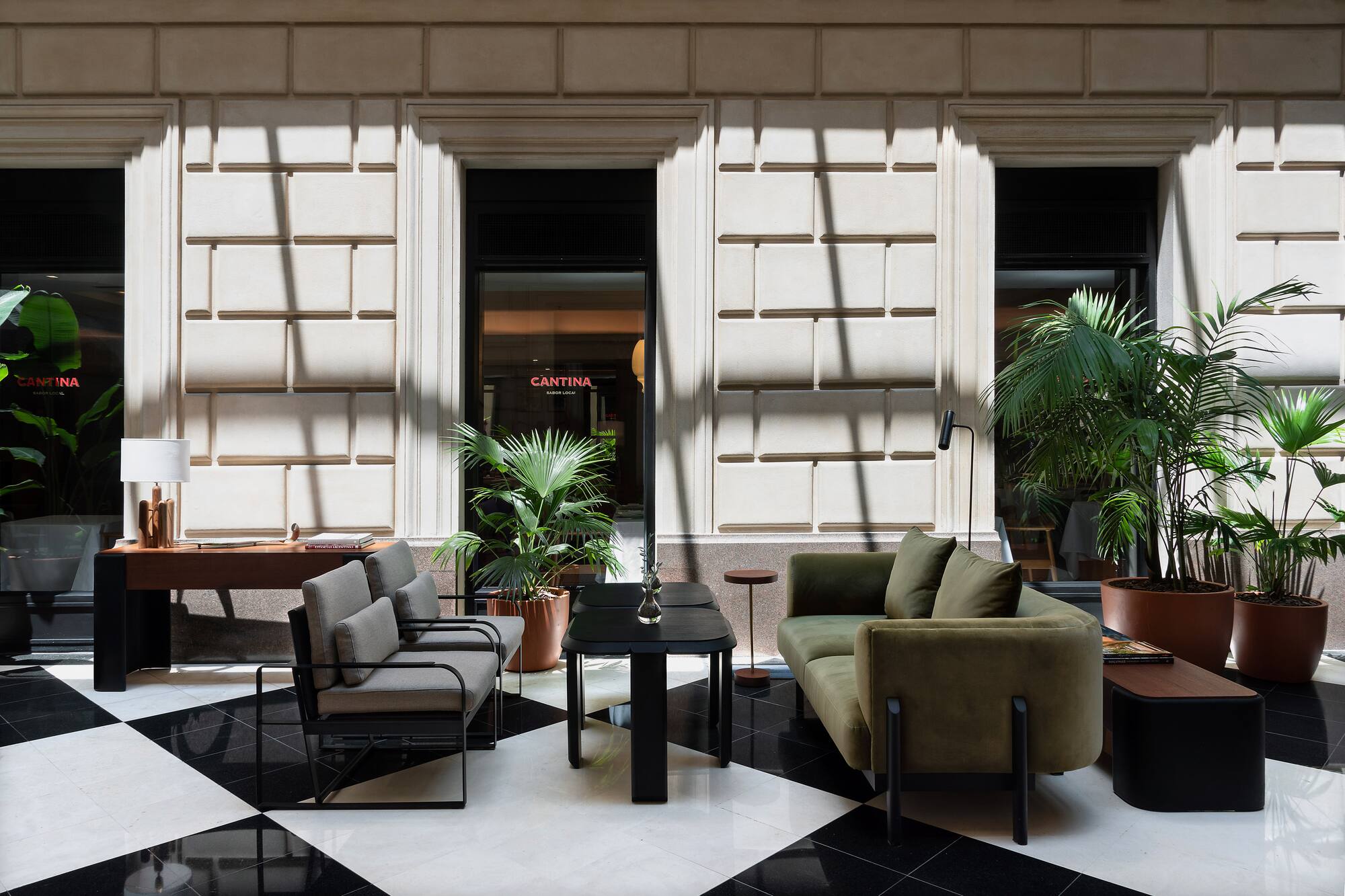 Modern lobby lounge with green sofa, plants, checkered floor, and Cantina sign.