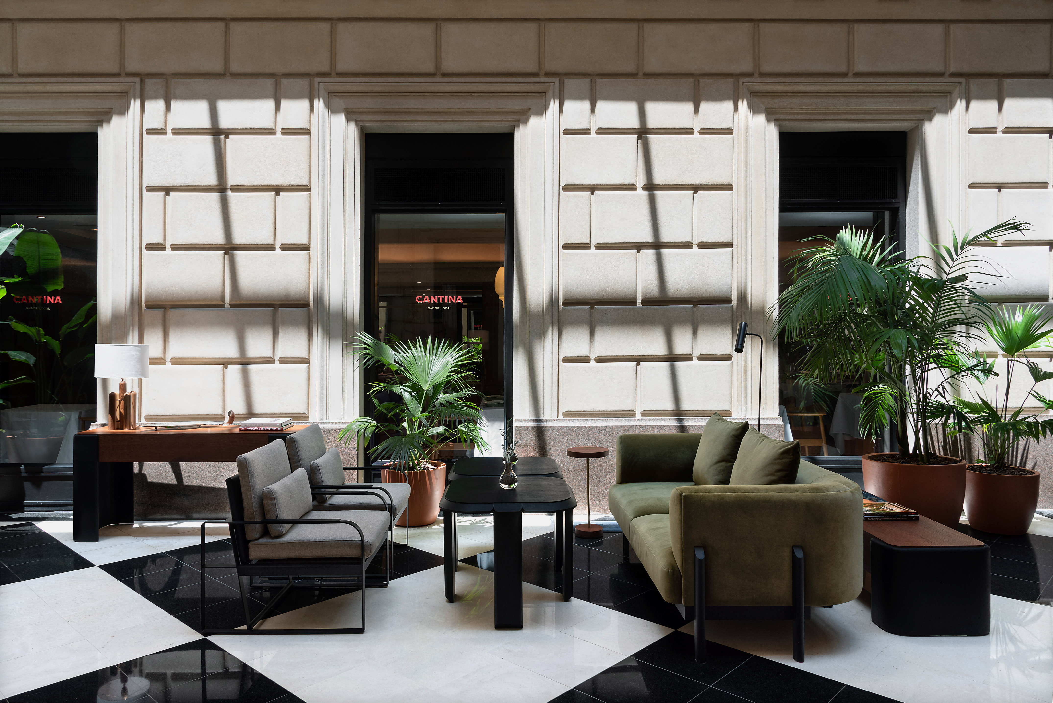 Modern lobby lounge with green sofa, plants, checkered floor, and Cantina sign.