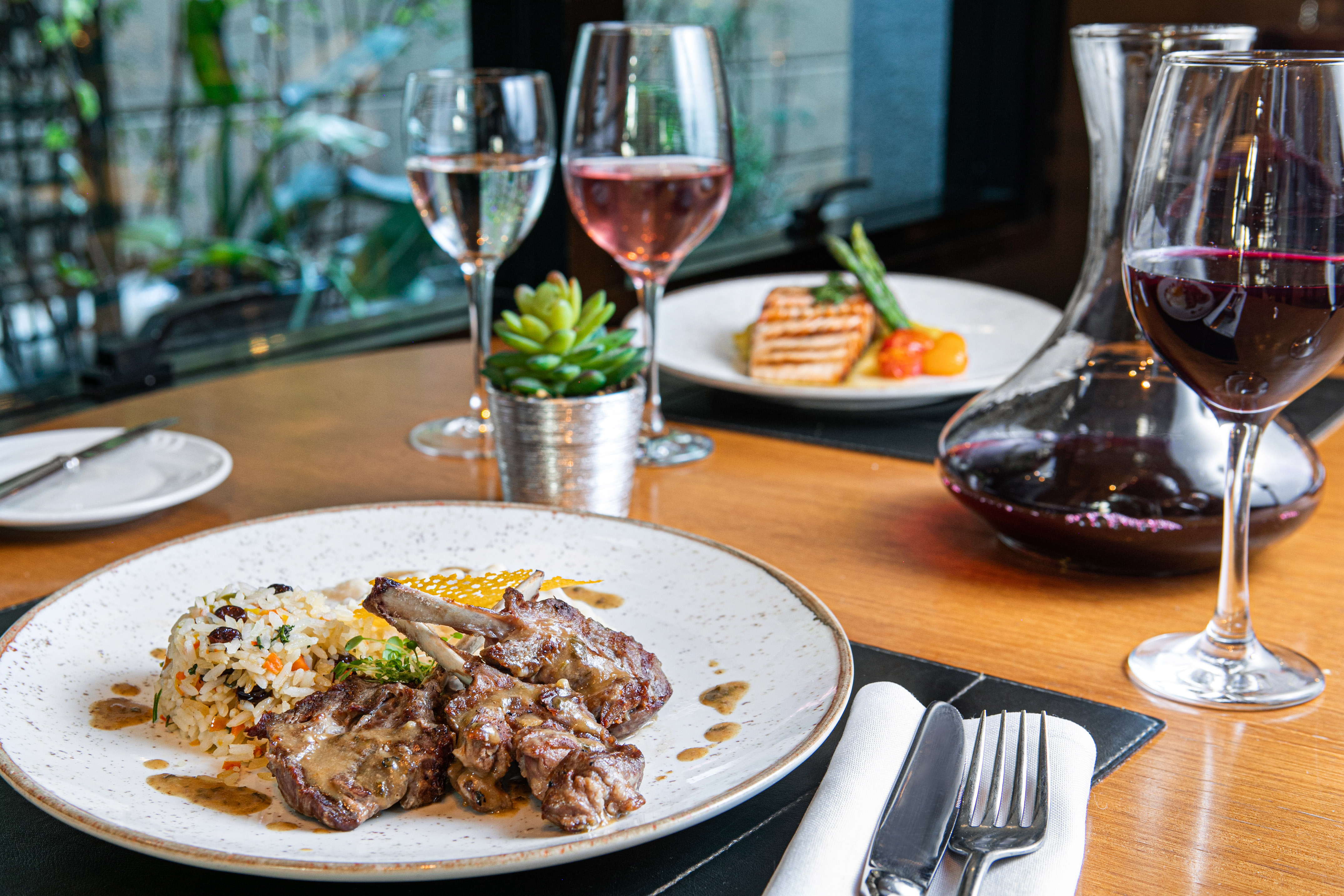 Gourmet lamb chops, rice, and grilled fish with wines on a restaurant table.