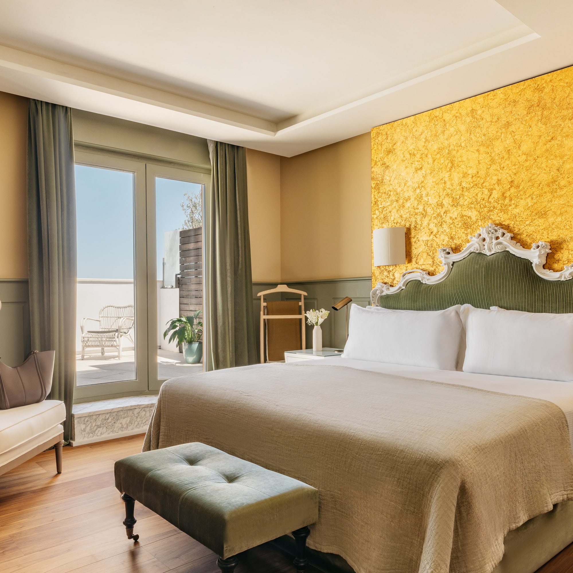 Lujosa suite de hotel con cama, cabecero verde, pared dorada y balcón.