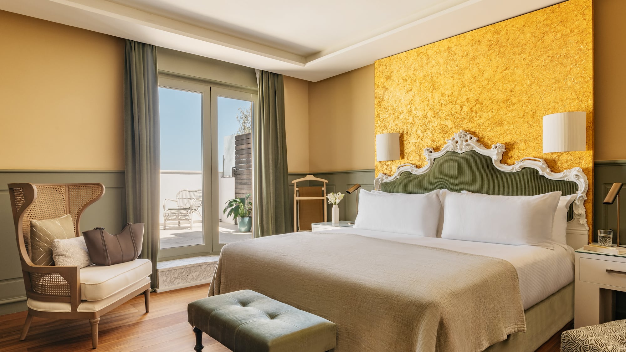 Lujosa suite de hotel con cama, cabecero verde, pared dorada y balcón.