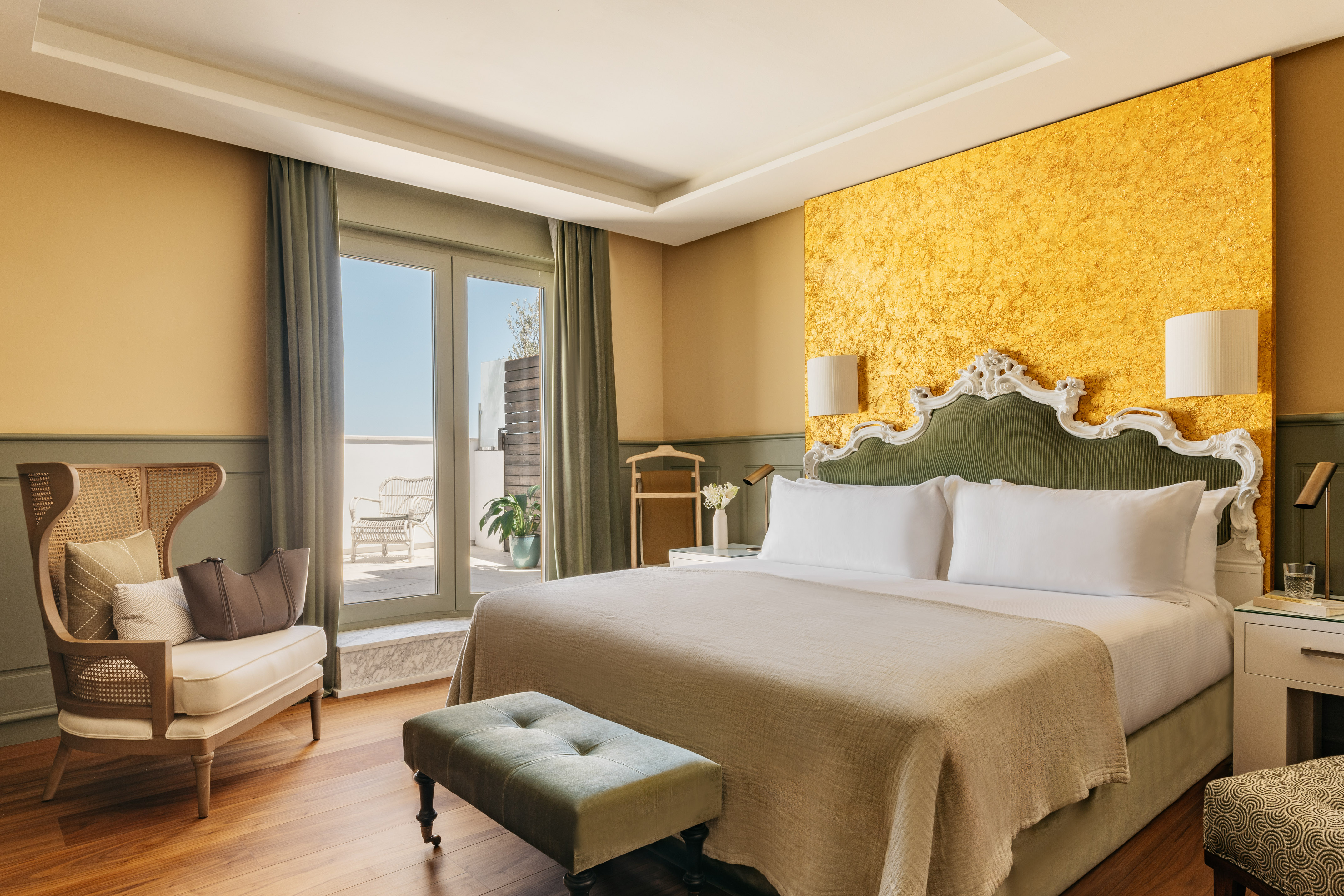 Lujosa suite de hotel con cama, cabecero verde, pared dorada y balcón.