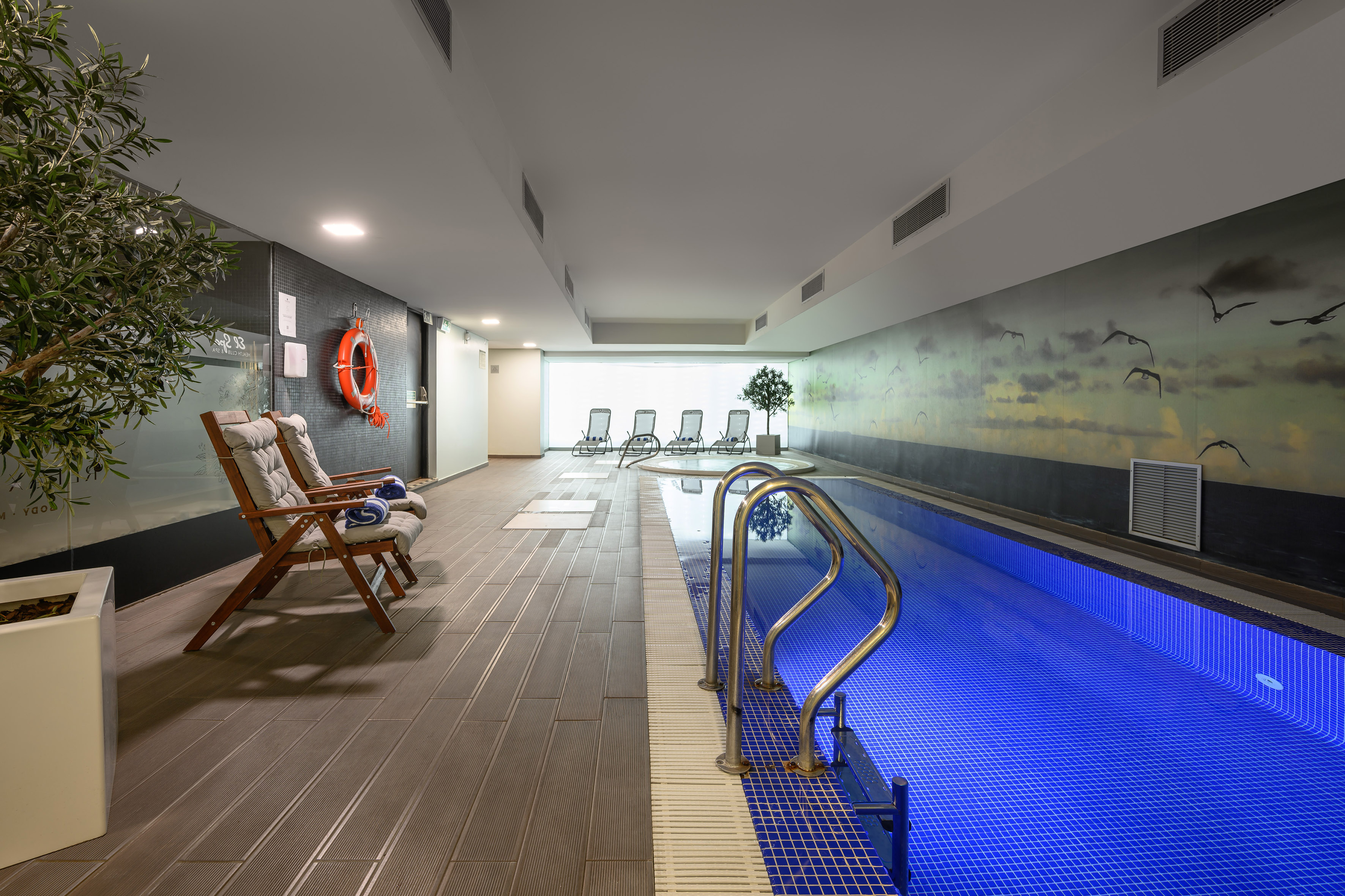 Contemporary indoor swimming pool and spa area with hot tub and lounge chairs.