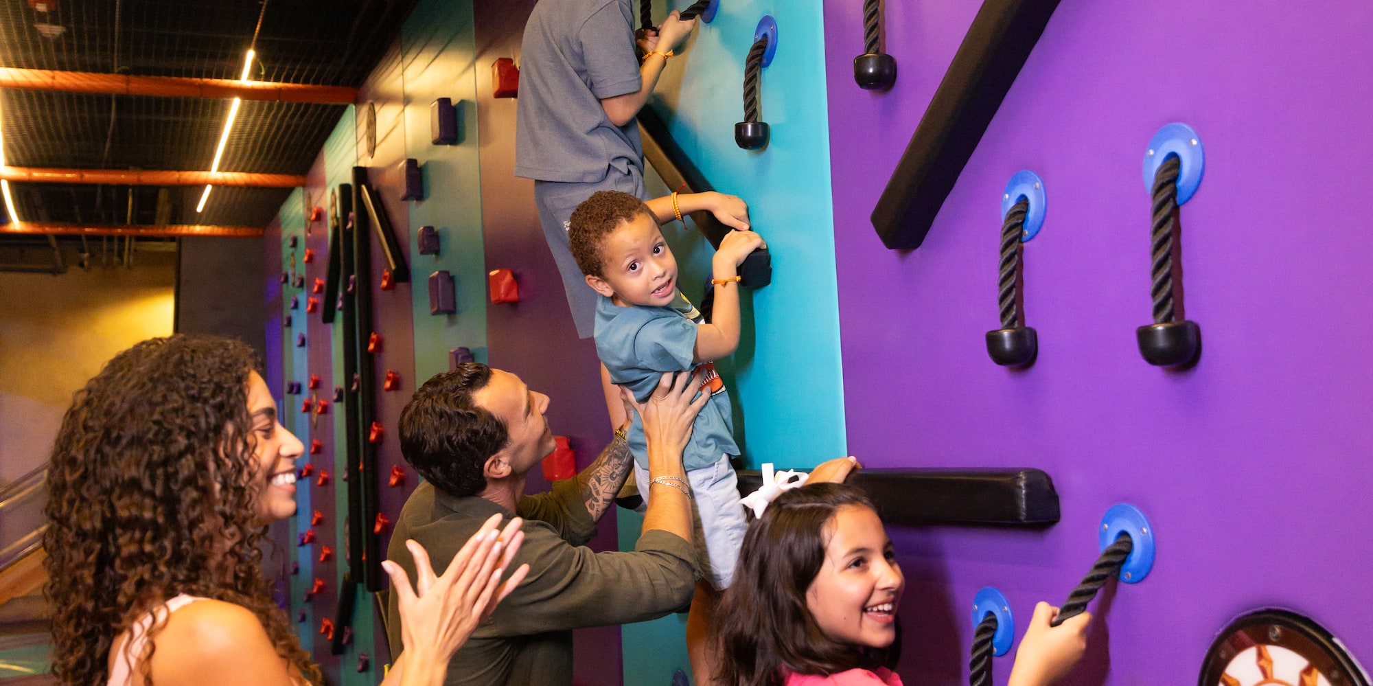 Kids and parents climb colorful indoor wall, active family fun.