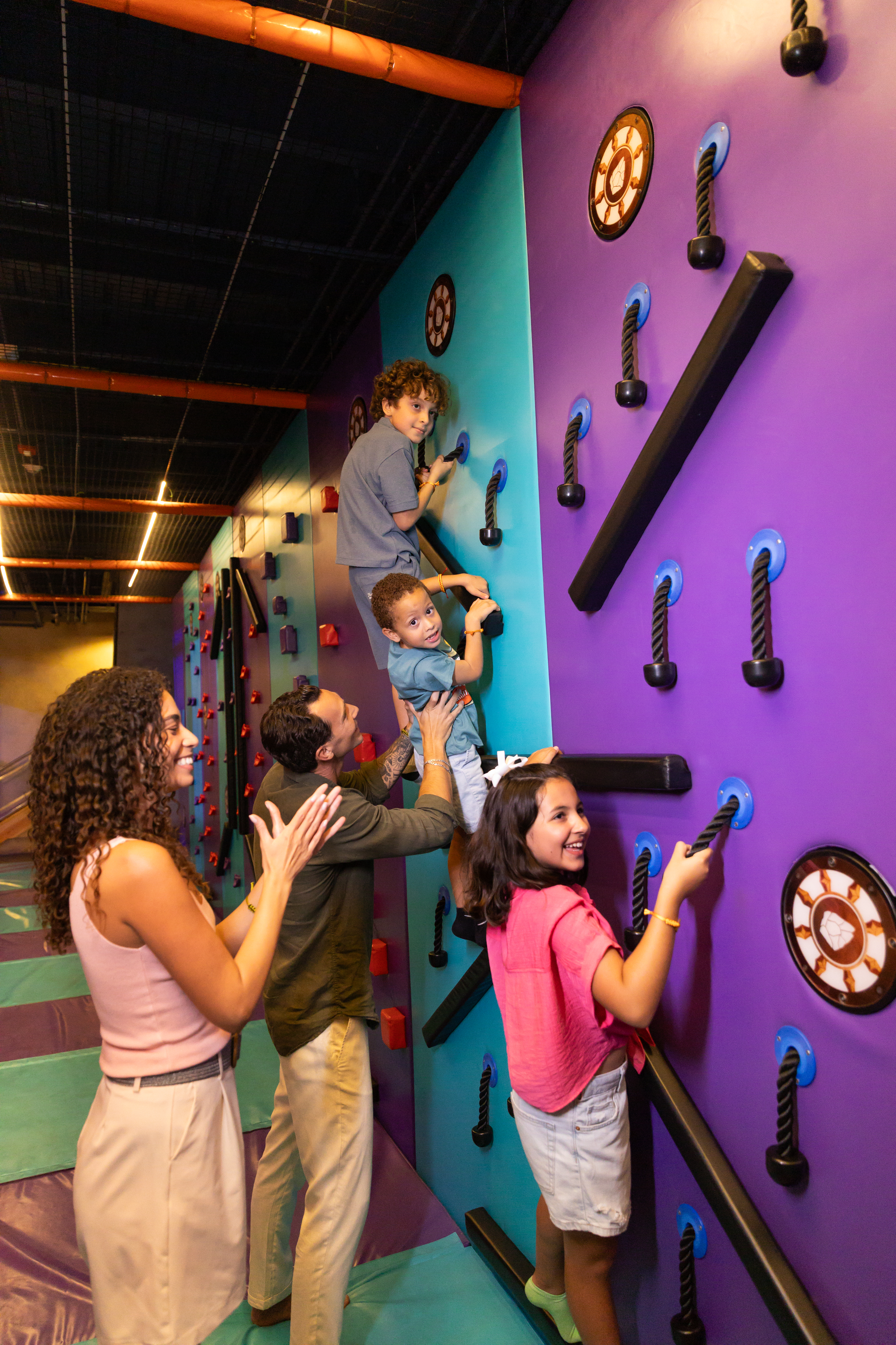 Kids and parents climb colorful indoor wall, active family fun.