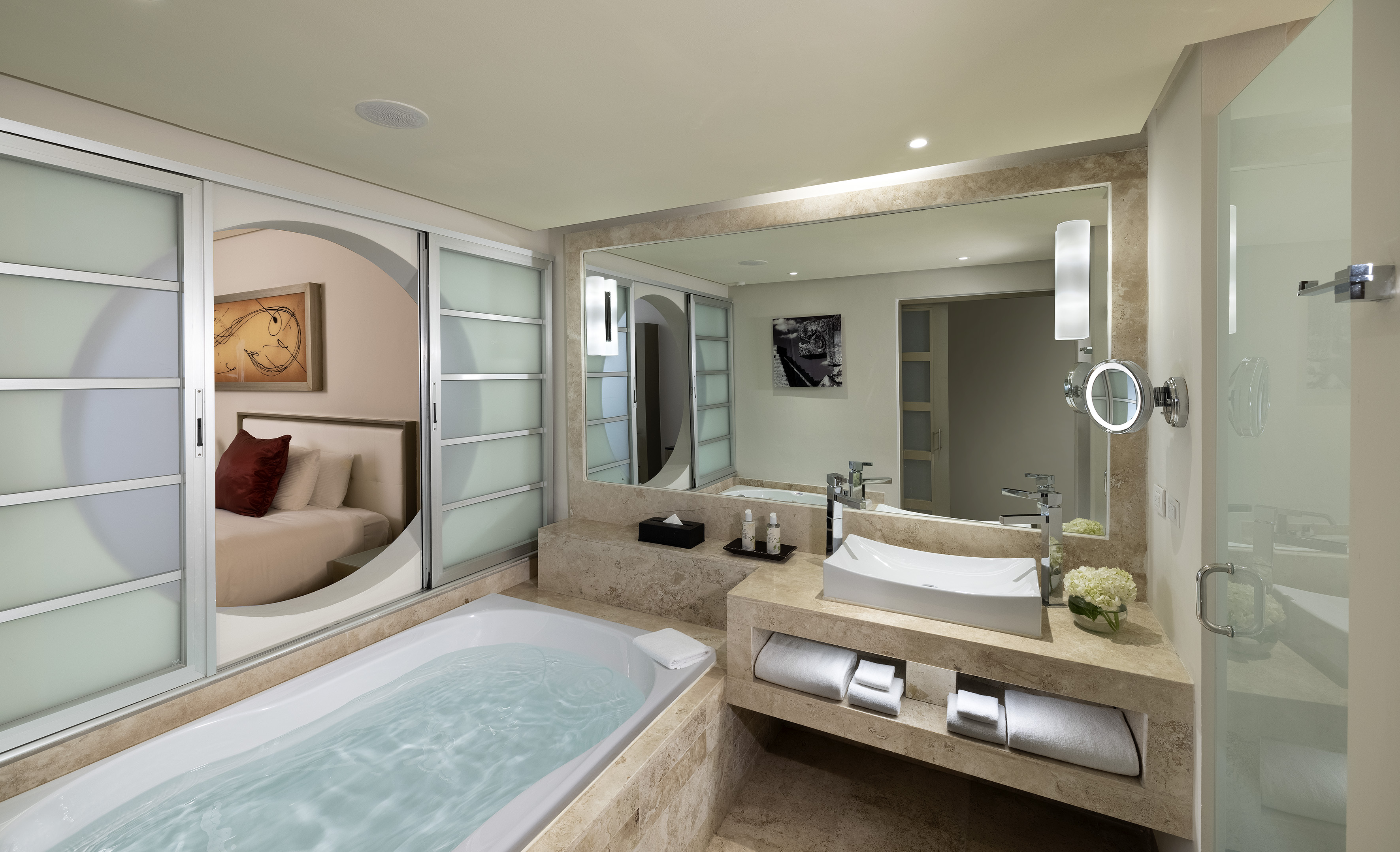 Hotel bathroom with large soaking tub, modern vanity, and bedroom access.