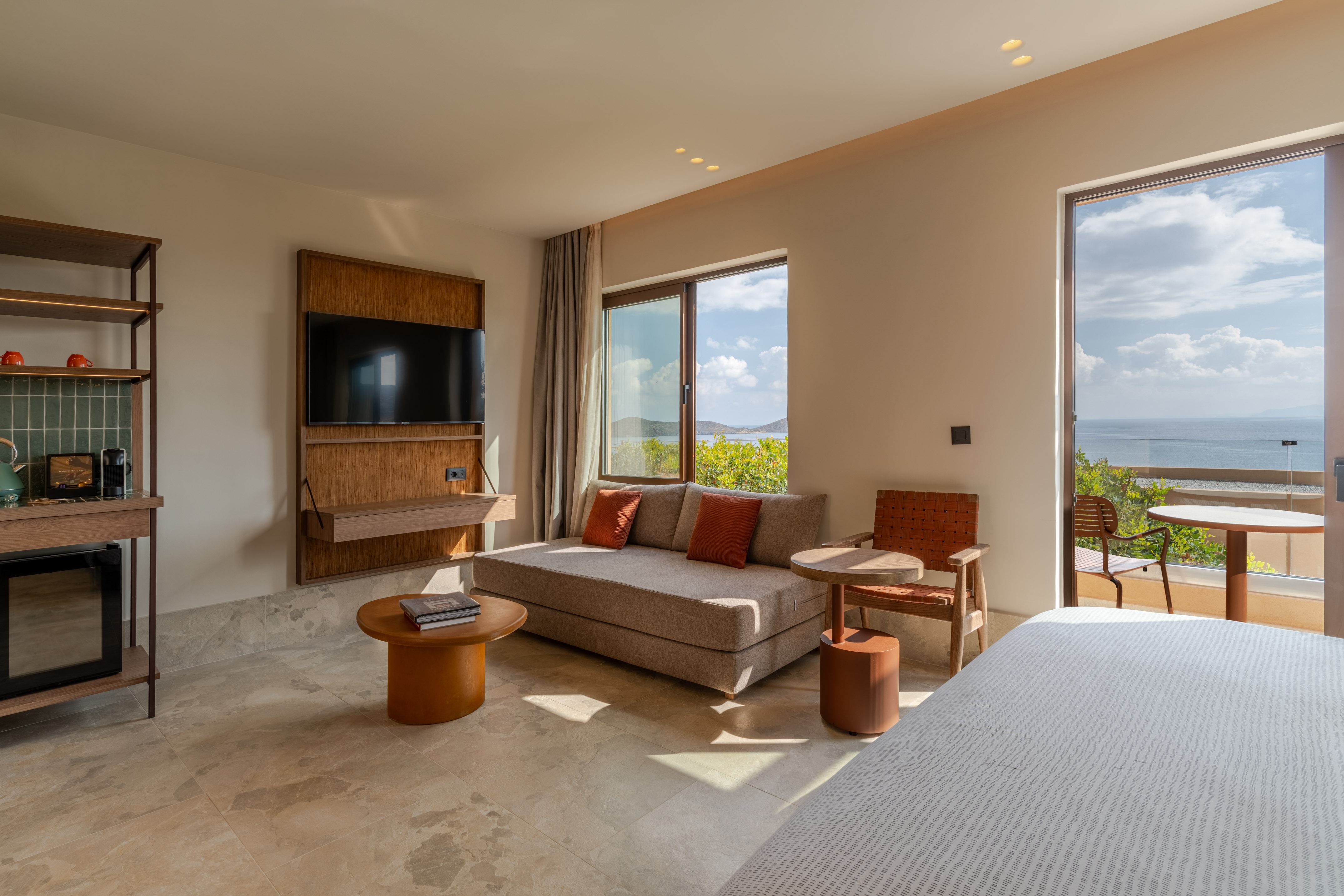 Luxury hotel suite with sea view balcony, modern living area, and TV.