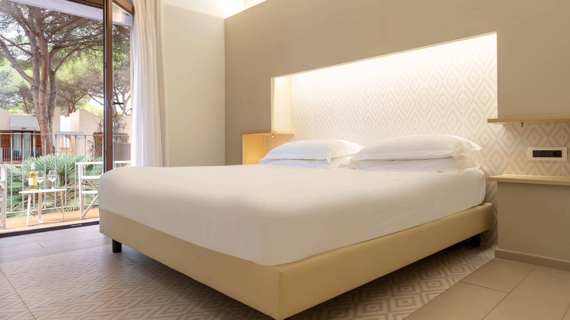 Spacious hotel bedroom with king bed, neutral decor, and balcony view of pine trees.