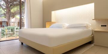 a bed with white sheets and pillows in a room with a glass door