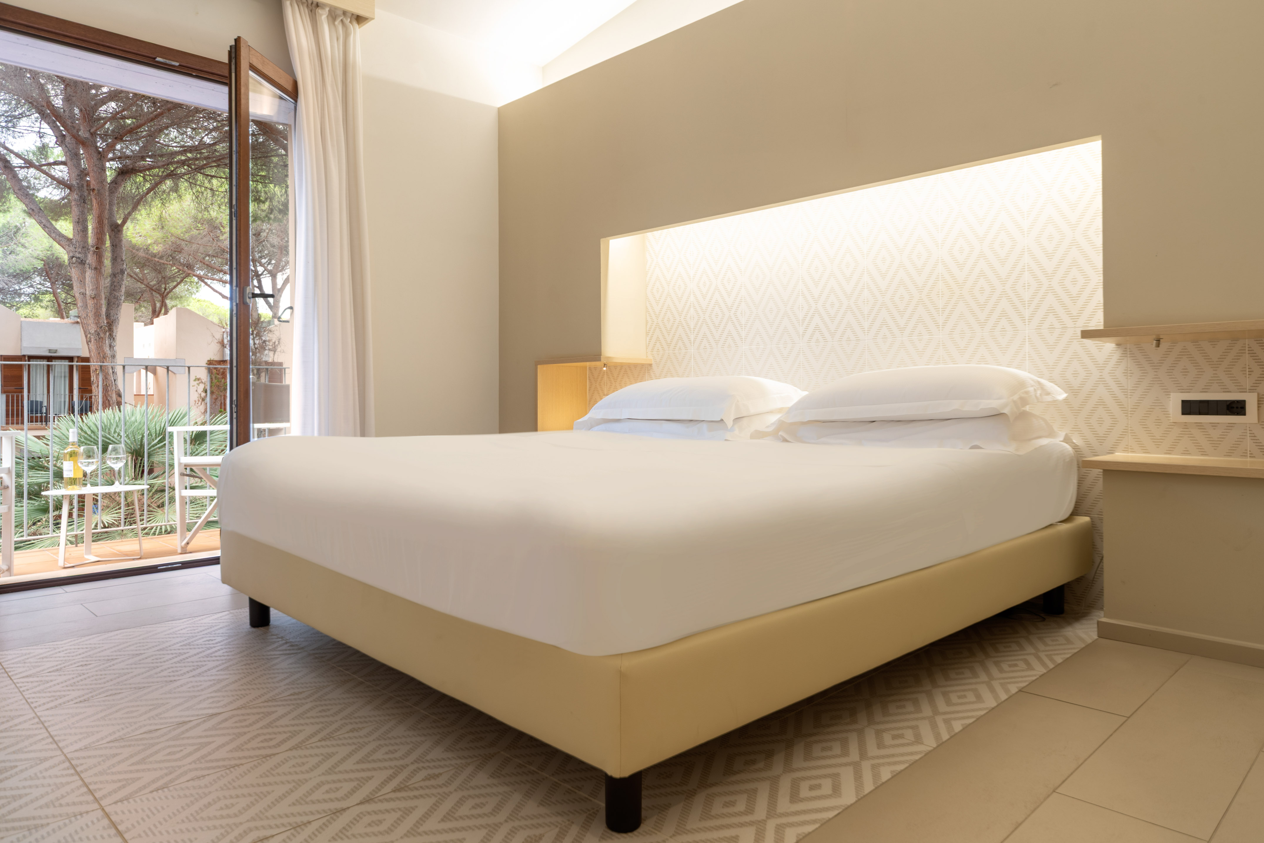 Spacious hotel bedroom with king bed, neutral decor, and balcony view of pine trees.