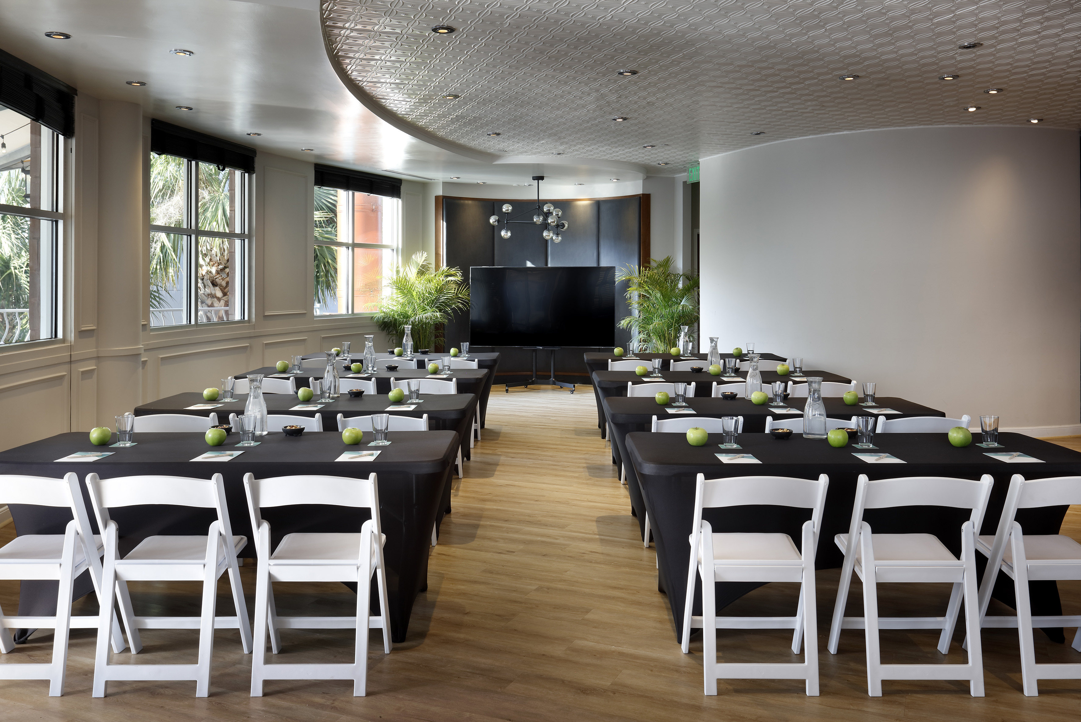 Modern meeting room with black tables, white chairs, apples, and screen. - The Pearl (circular floor plan) - Meliá Orlando Celebration, Orlando