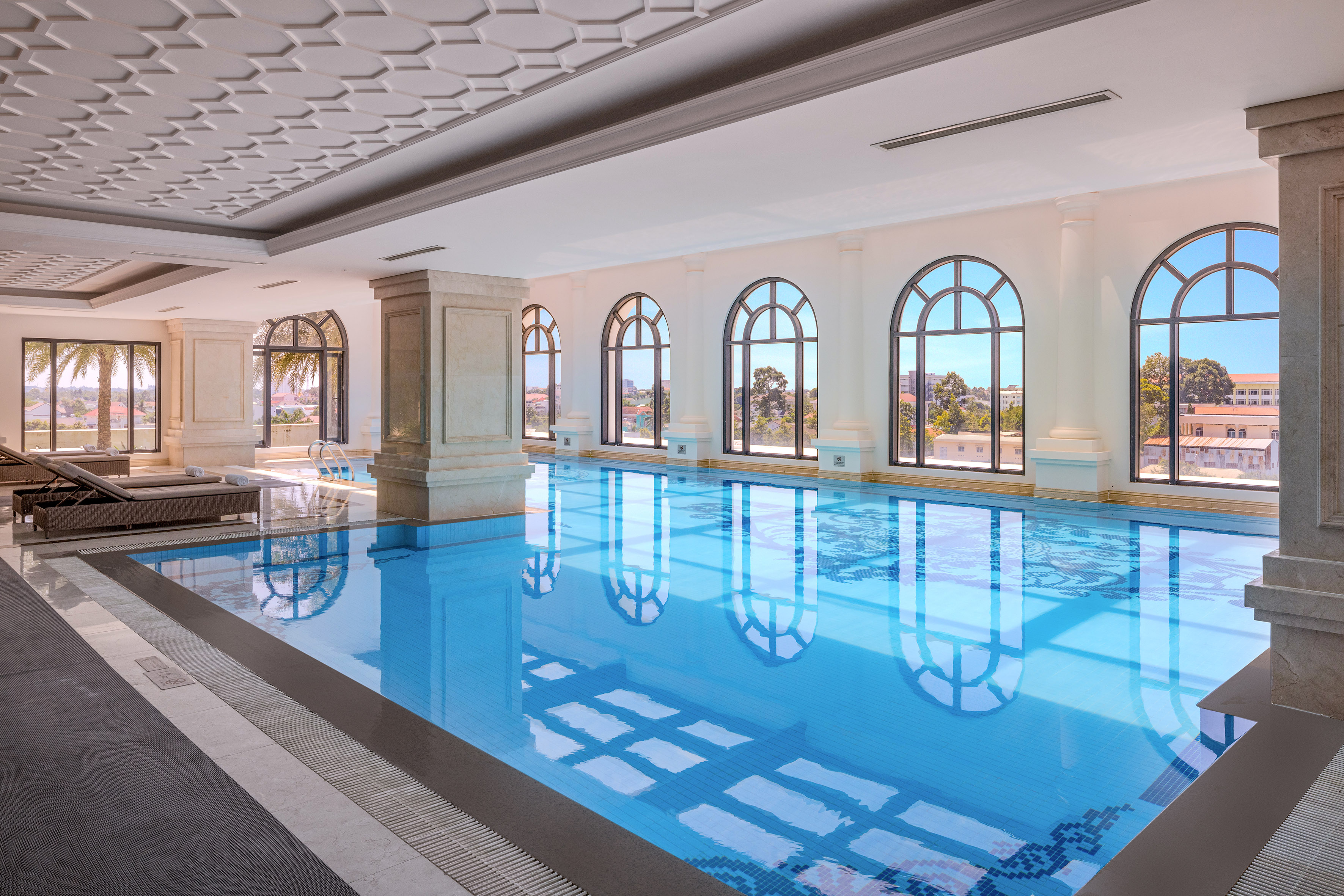 Elegant indoor swimming pool with arched windows and patterned ceiling.
