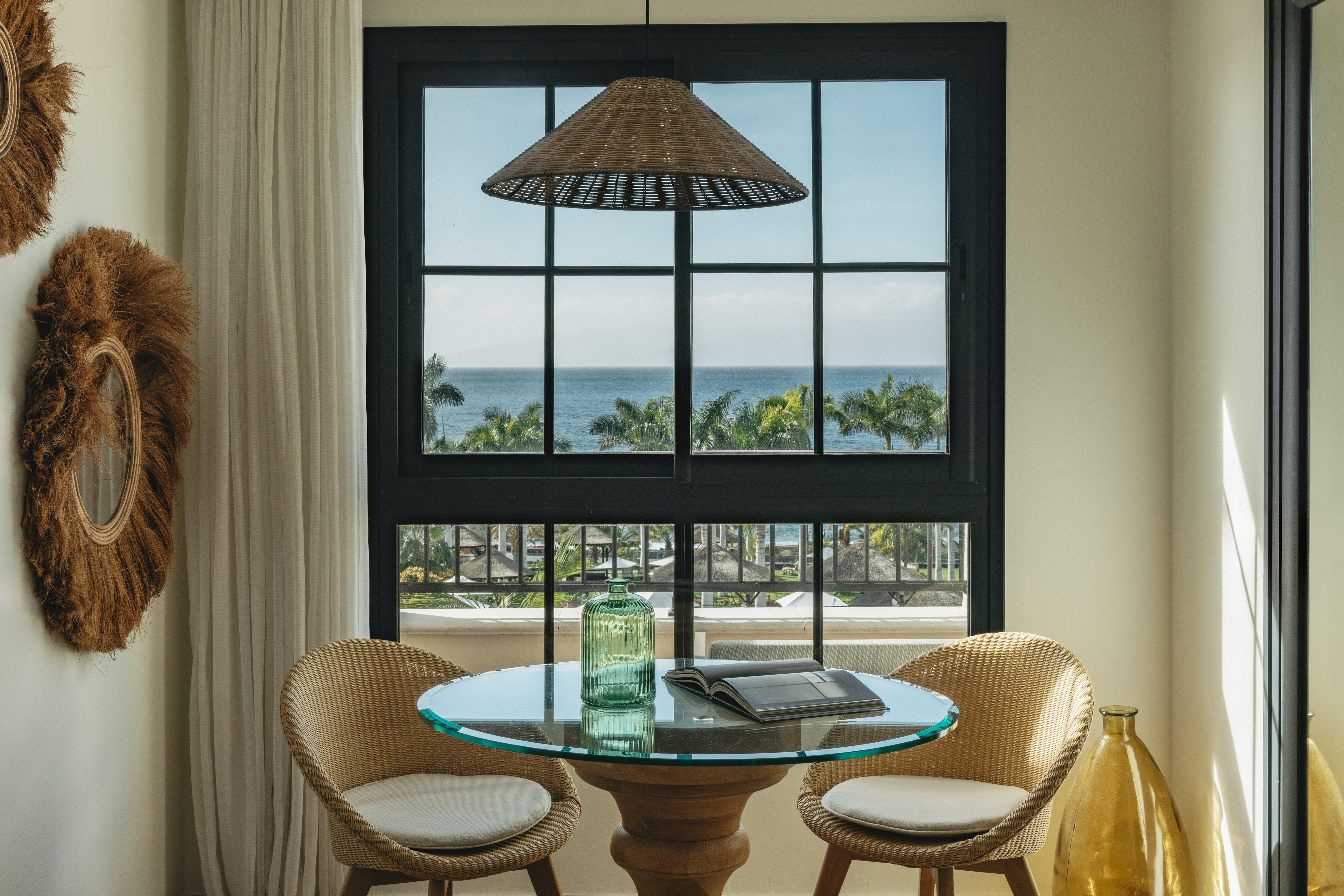 Oceanfront dining nook with tropical view, wicker chairs, glass table.