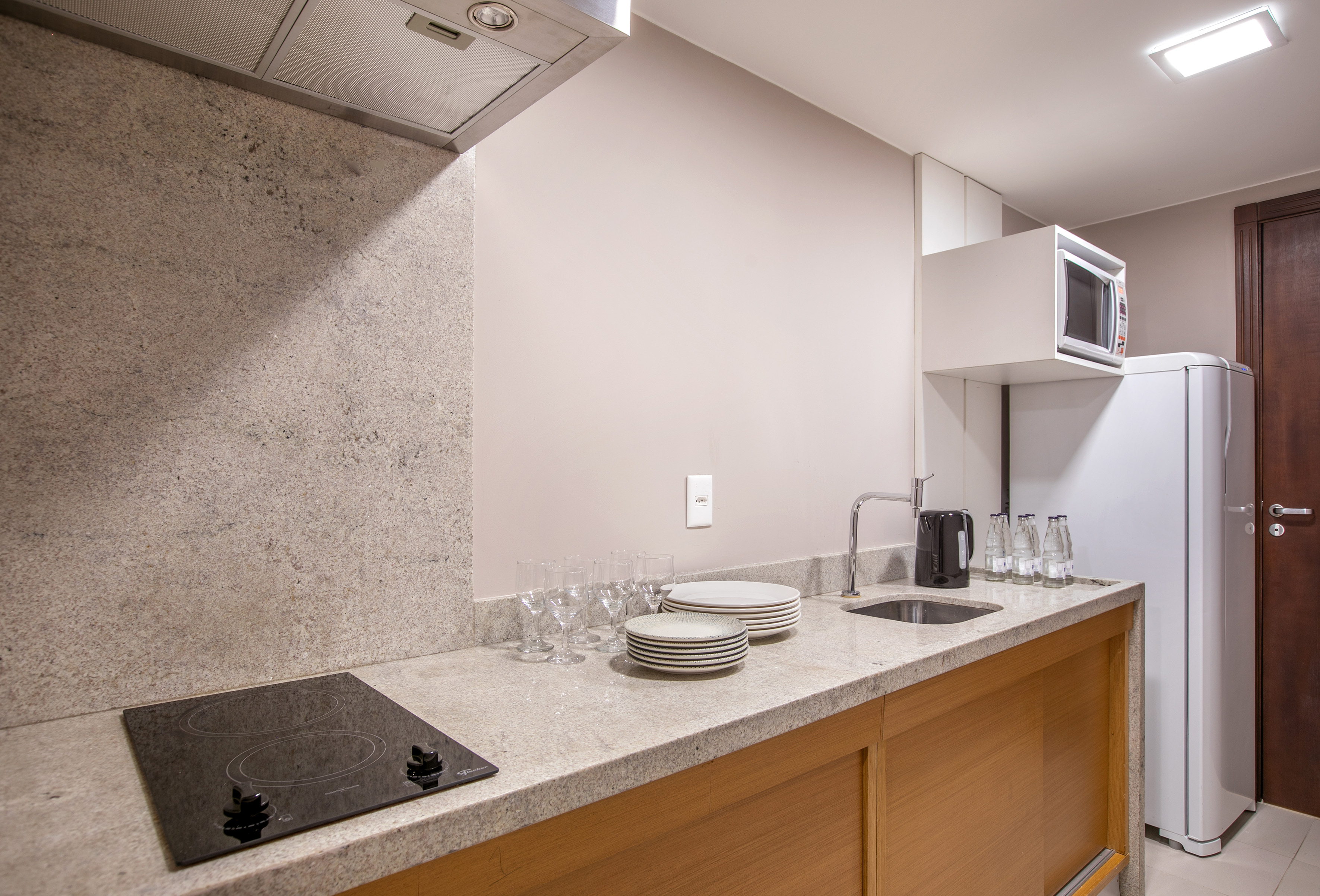 Modern kitchenette with granite counter, cooktop, microwave, and fridge.
