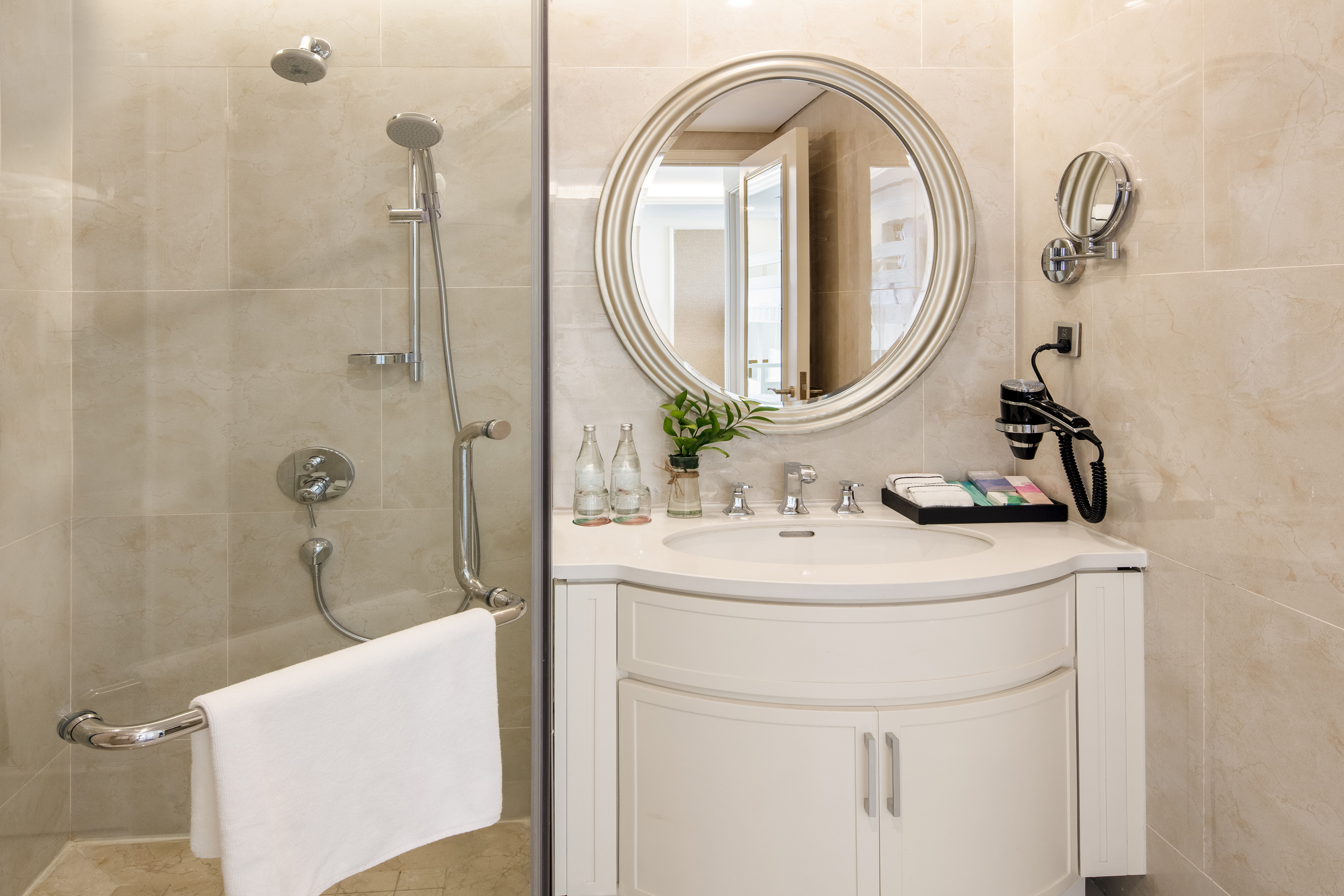 Modern hotel bathroom with shower, vanity, oval mirror, and hairdryer.