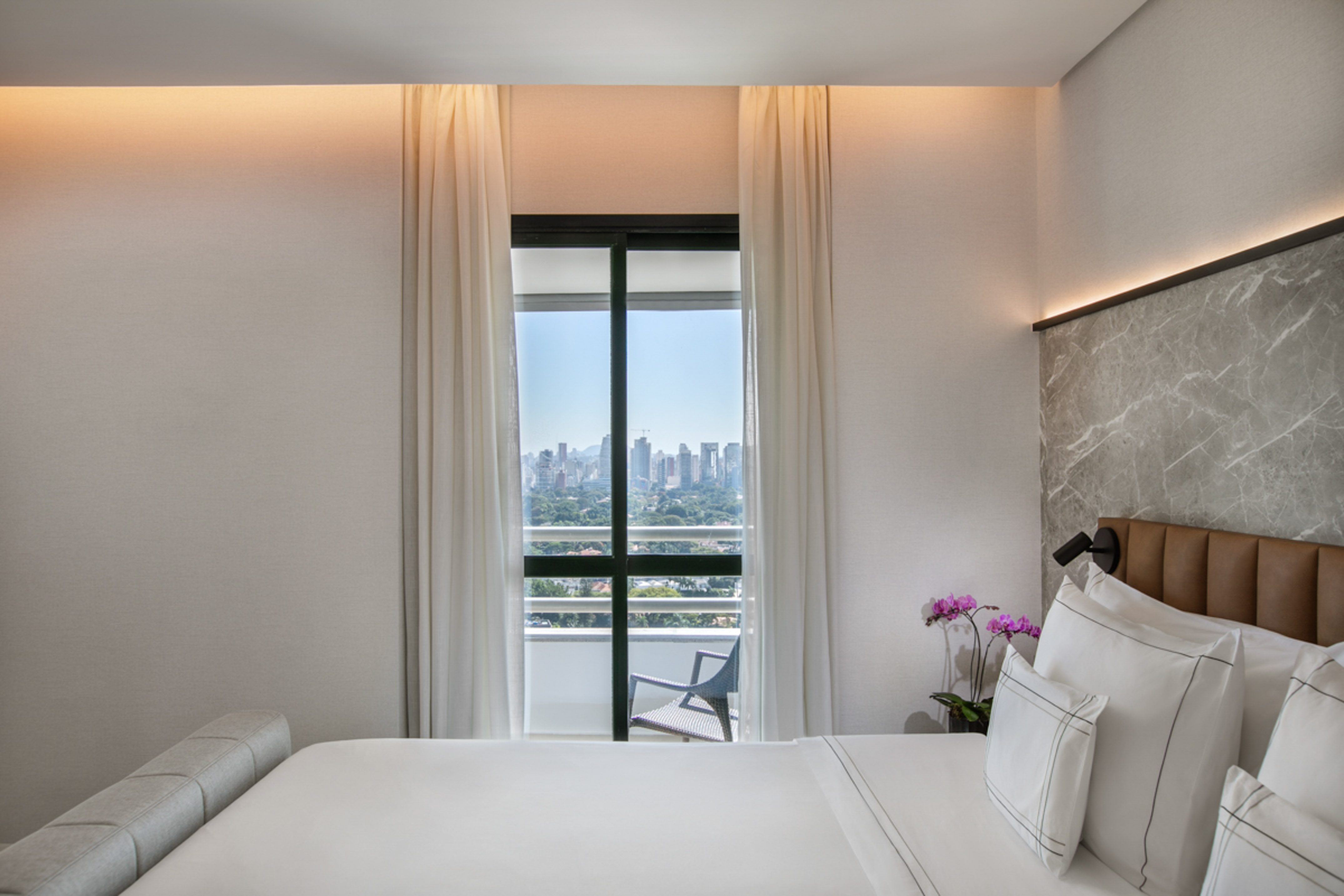 Modern hotel bedroom with city skyline view from a balcony.