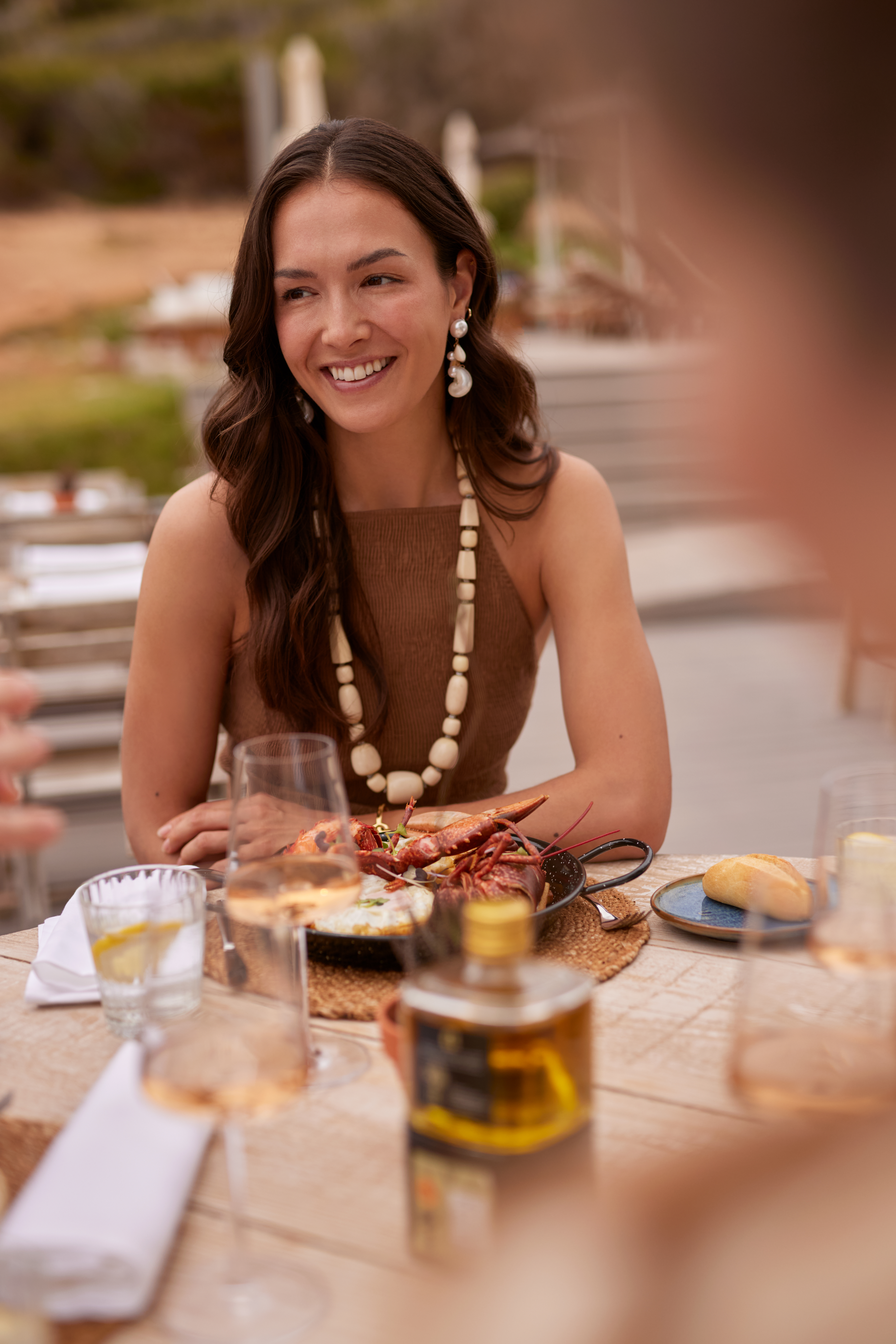 Smiling woman at an outdoor restaurant table, enjoying lobster and wine.