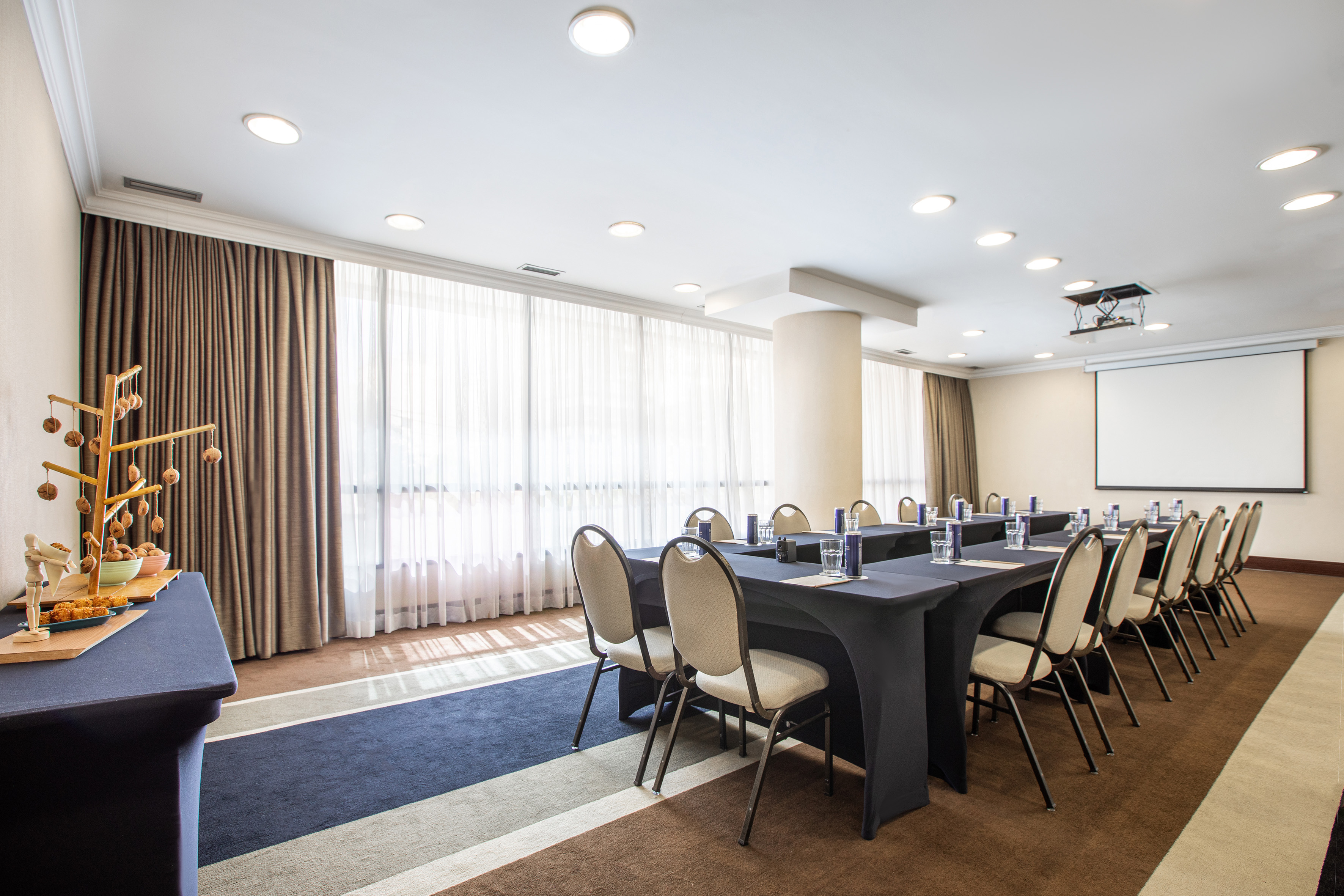 Business meeting room with conference tables, projector screen, and snack bar.