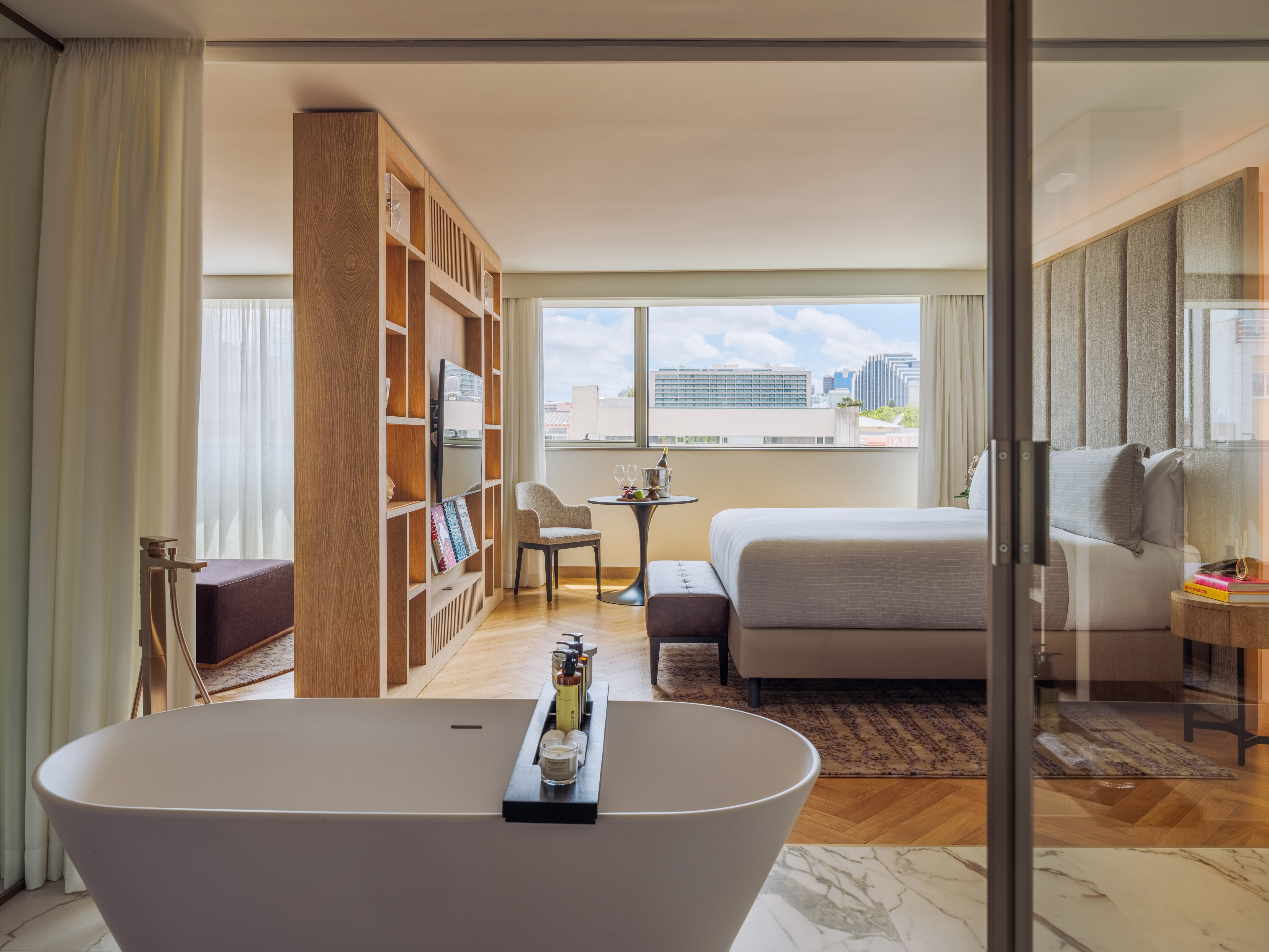 Luxury hotel suite with freestanding tub, modern bedroom, and city view.
