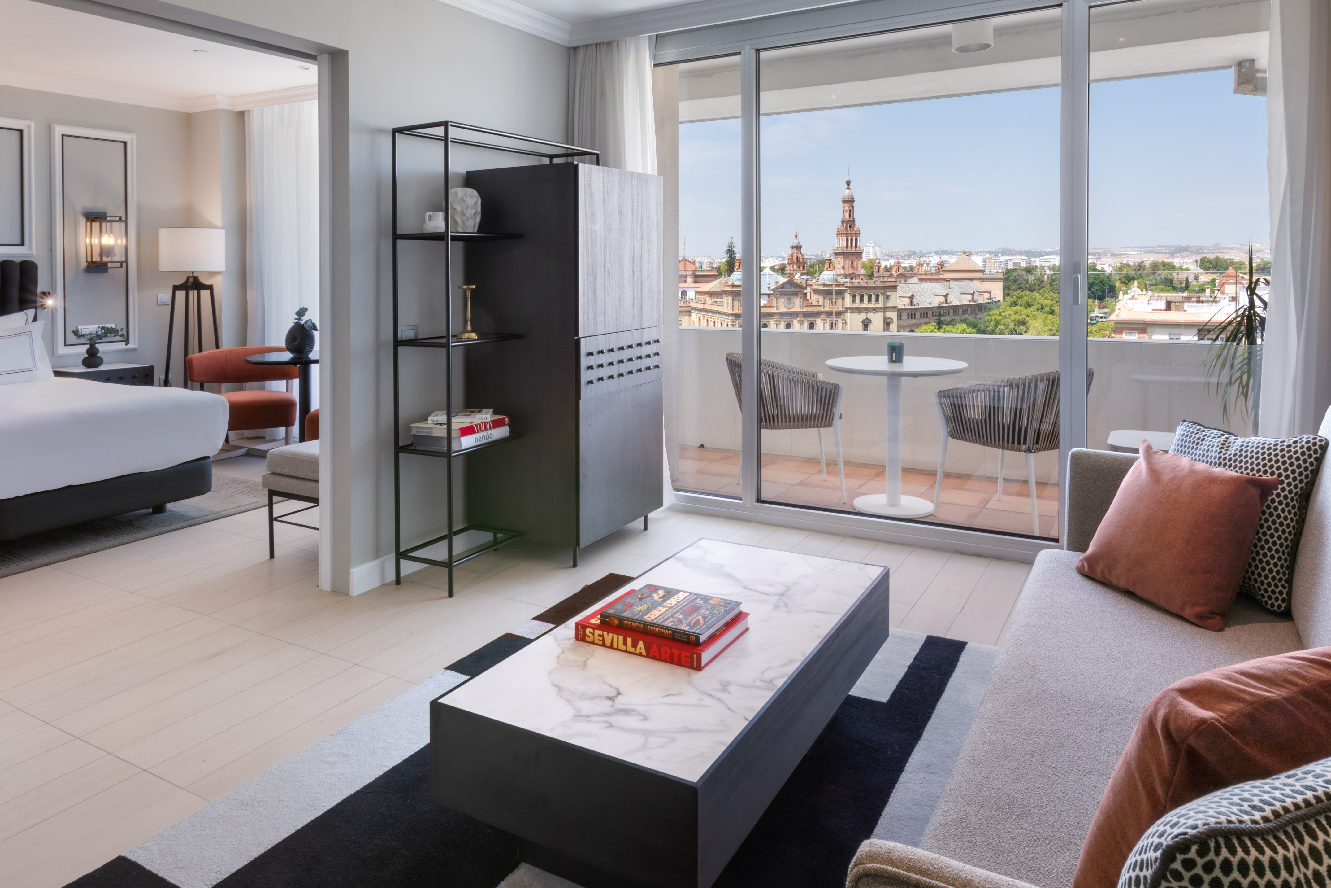 Modern hotel suite with living room, balcony, and Seville city view.
