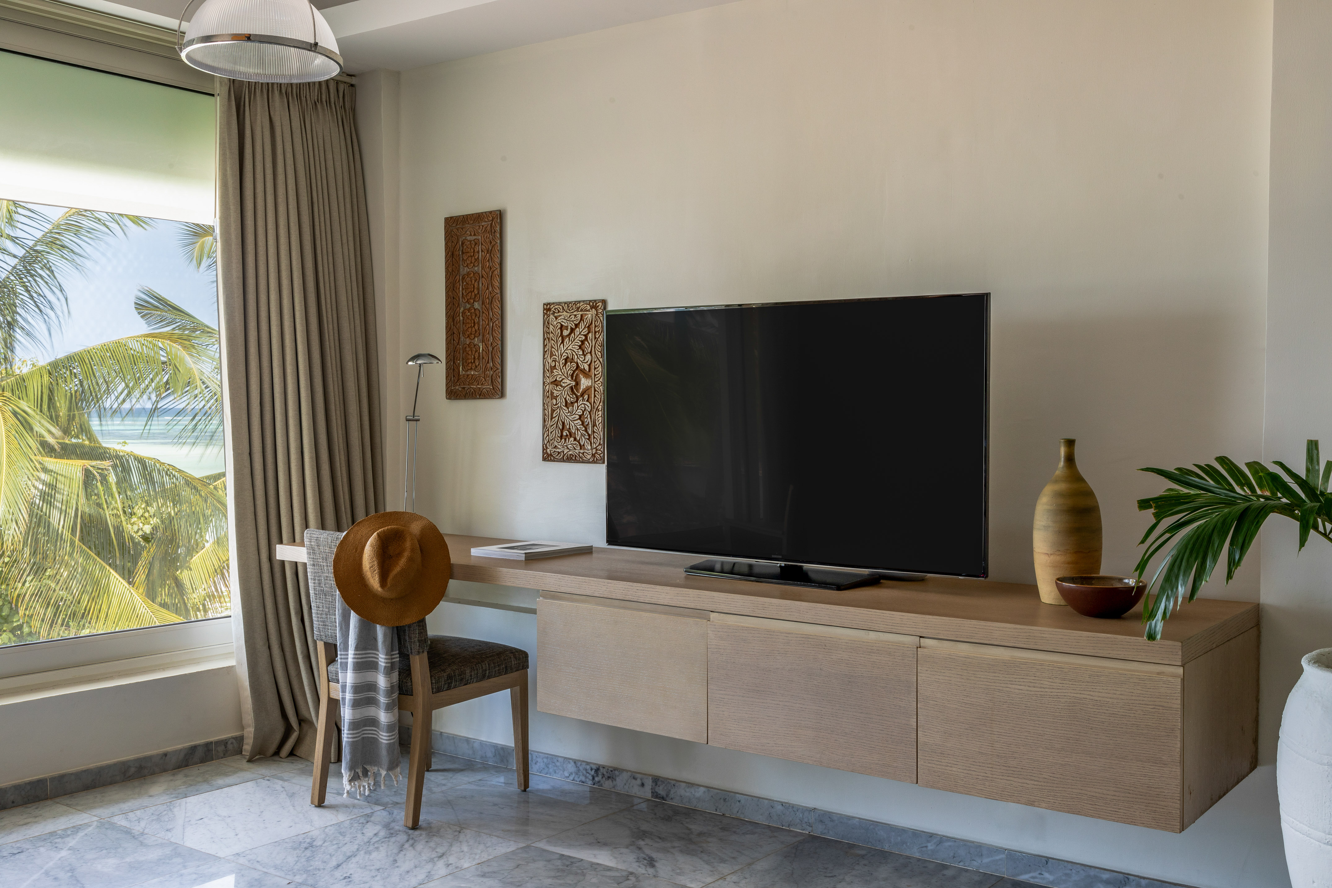 Tropical room with ocean view, palm trees, modern TV console, and desk.