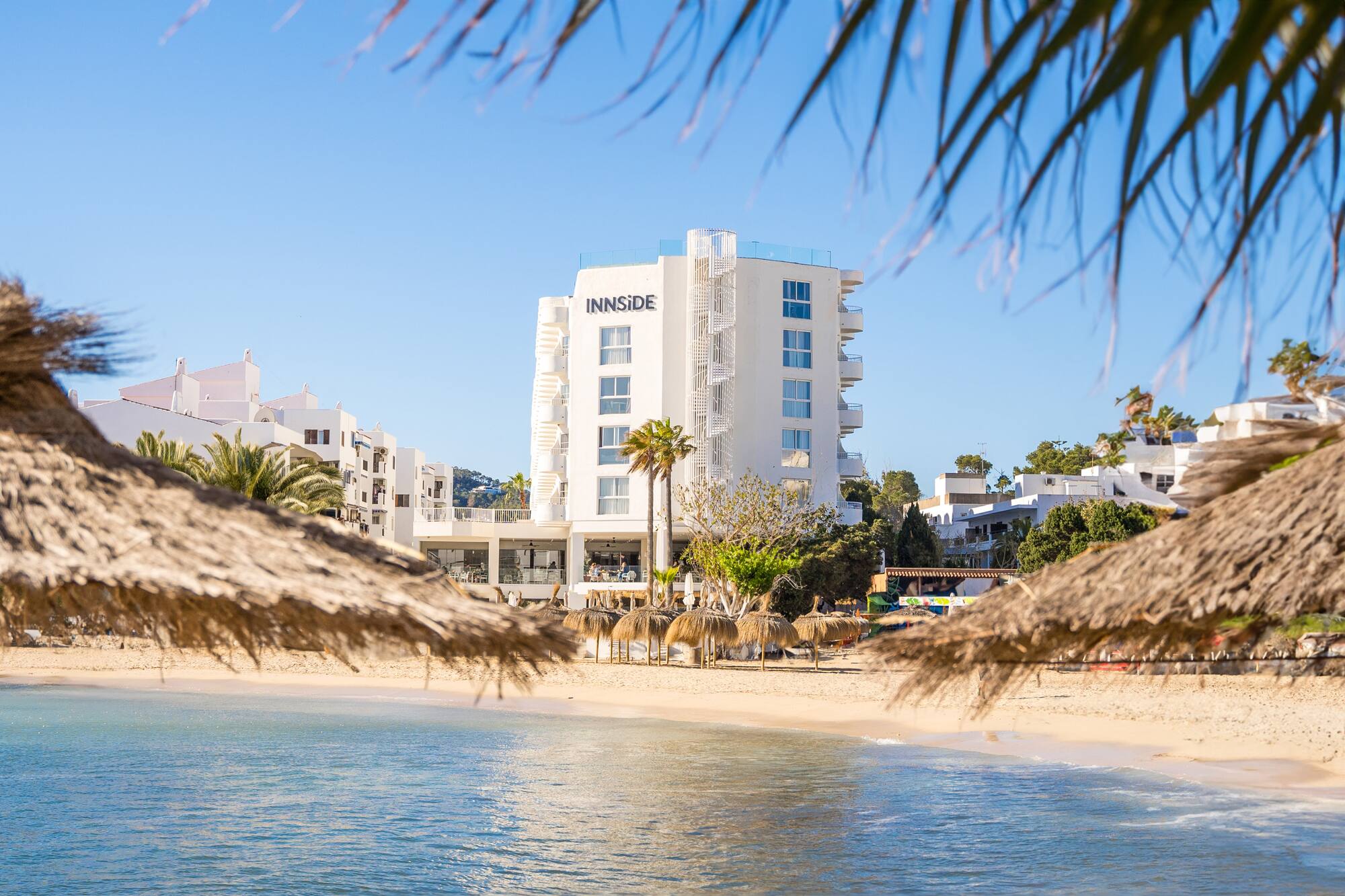 White INNSIDE hotel beachfront with straw umbrellas and blue sea.