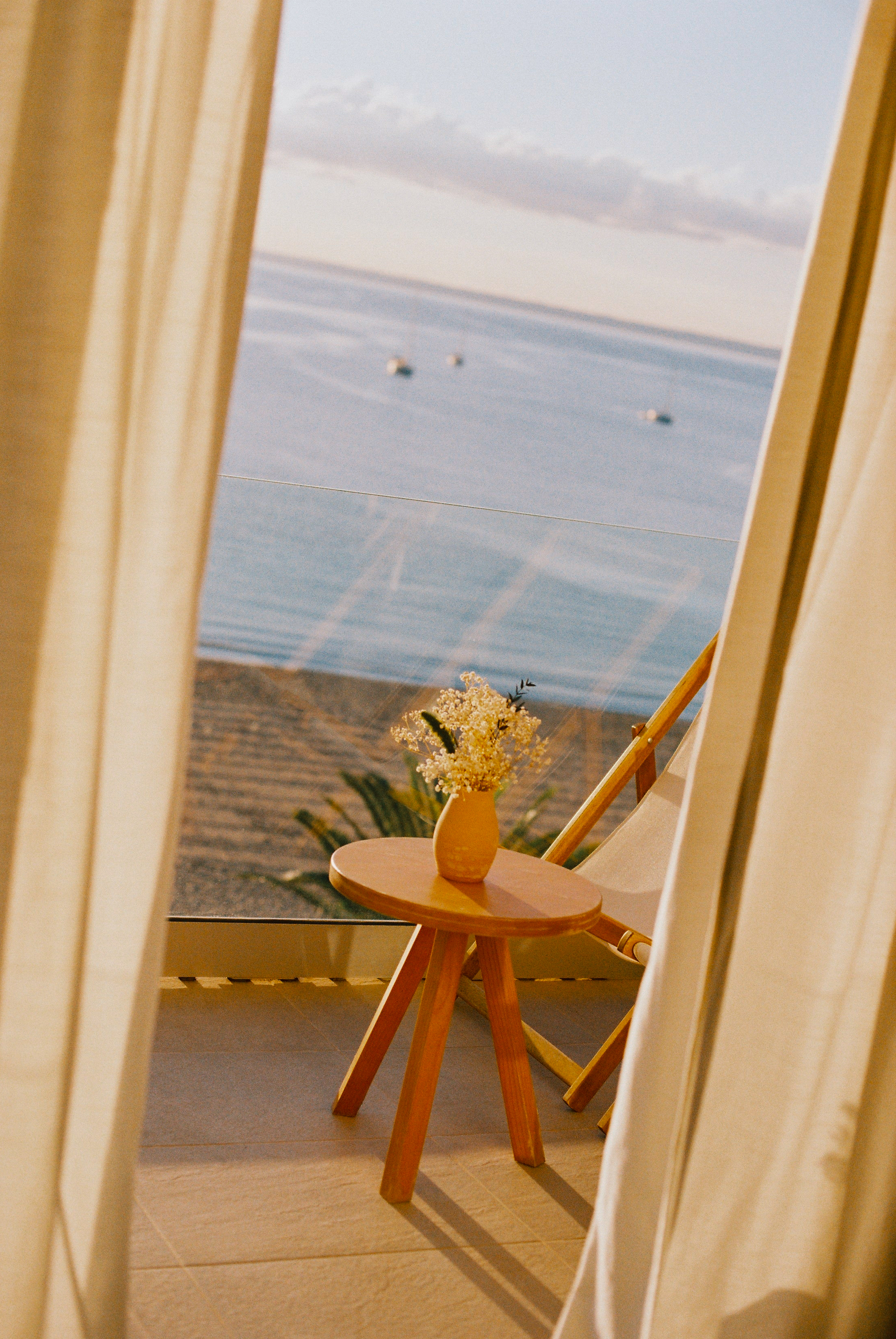Balcony ocean view with flowers on table, lounge chair, and beach.