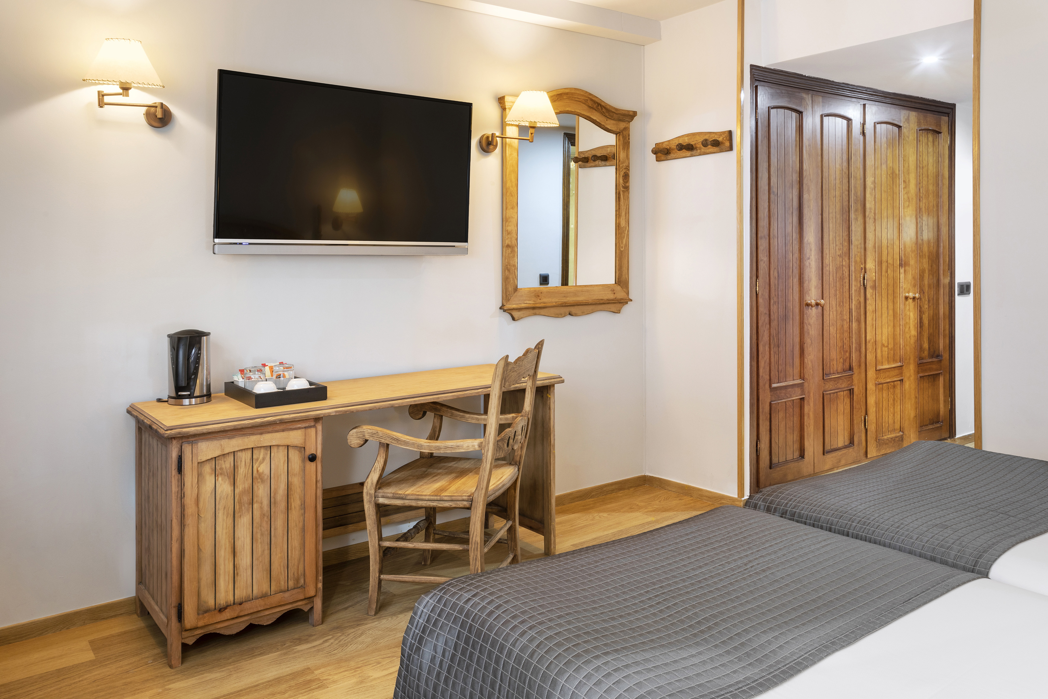 Hotel guest room with rustic wooden desk, TV, mirror, and twin beds.