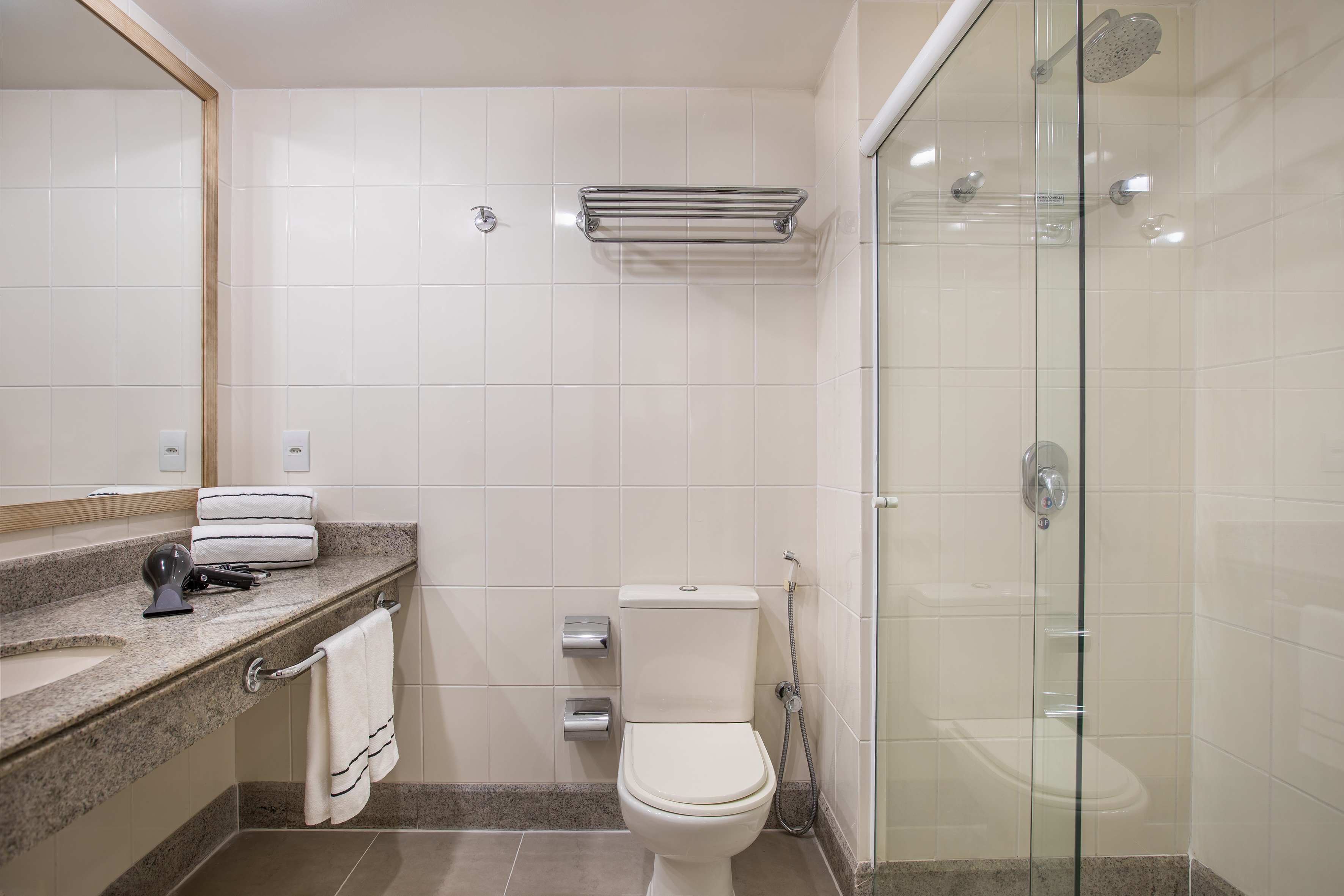 Clean hotel bathroom featuring white tiles, granite counter, toilet, and glass shower.