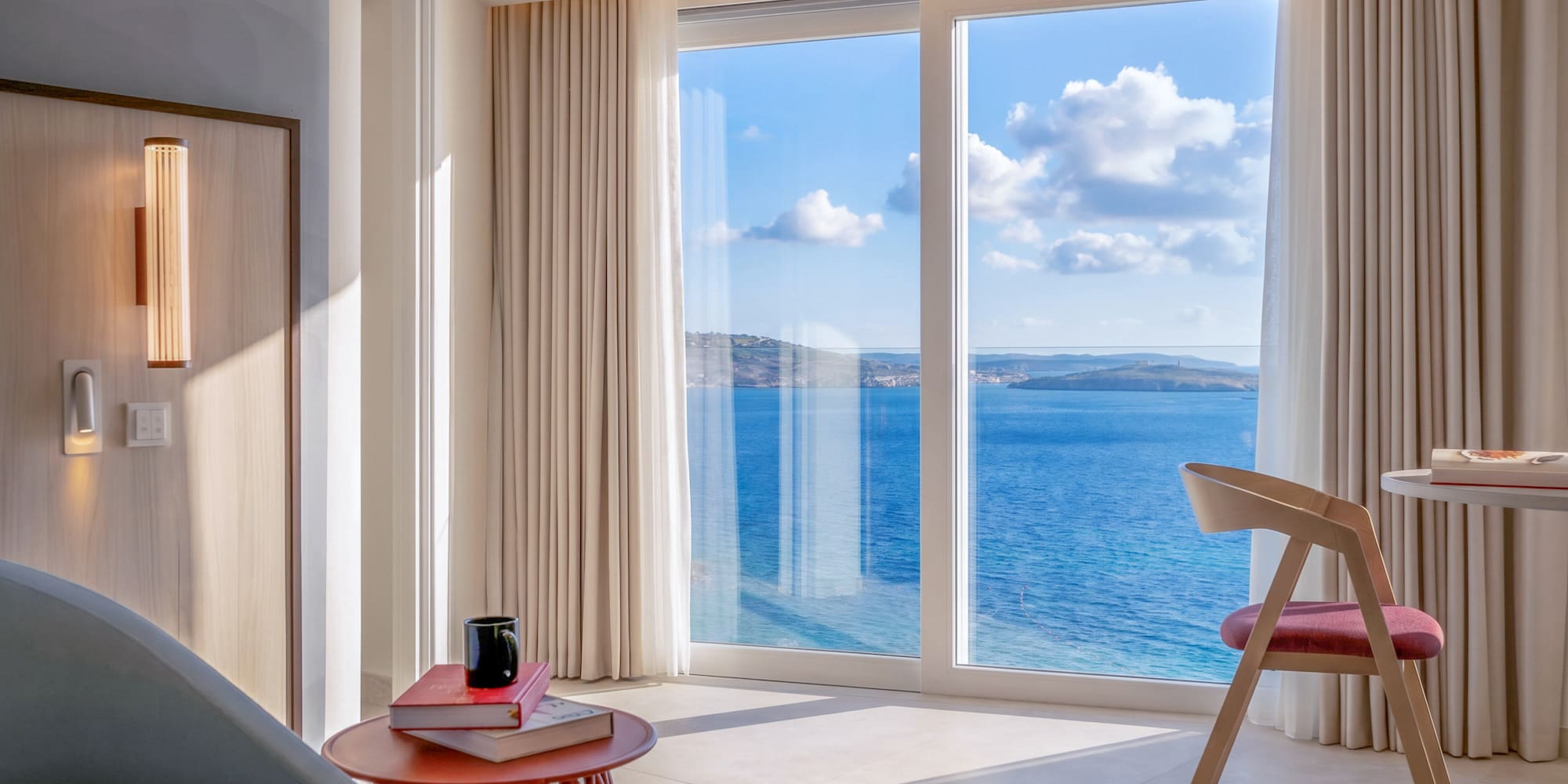 Bright modern hotel room with panoramic sea view from large window.