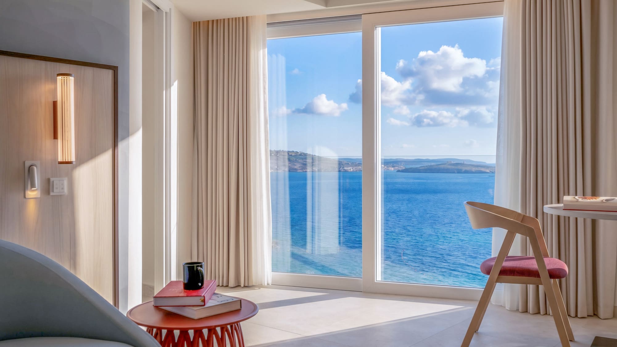 Bright modern hotel room with panoramic sea view from large window.