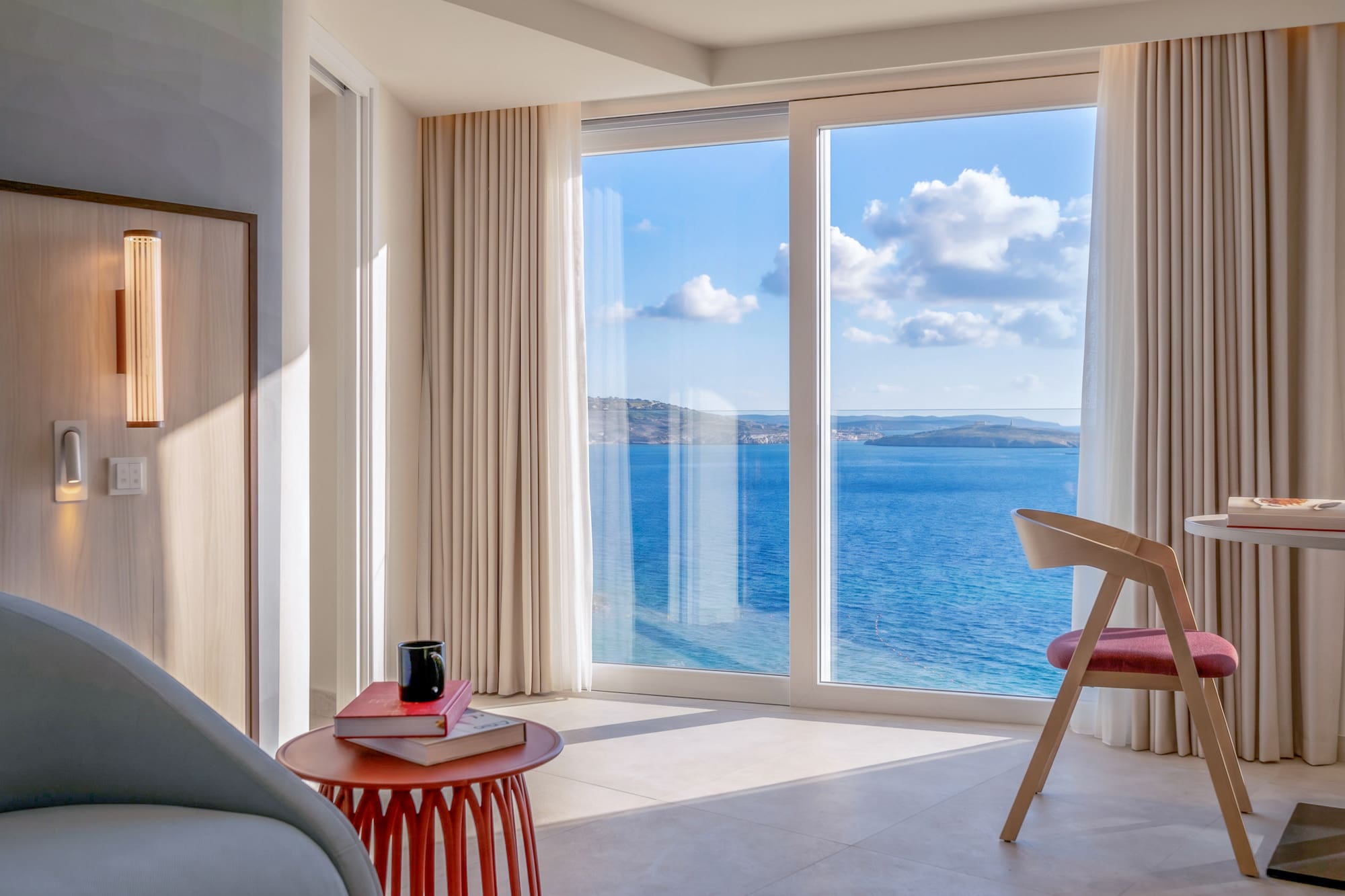 Bright modern hotel room with panoramic sea view from large window.