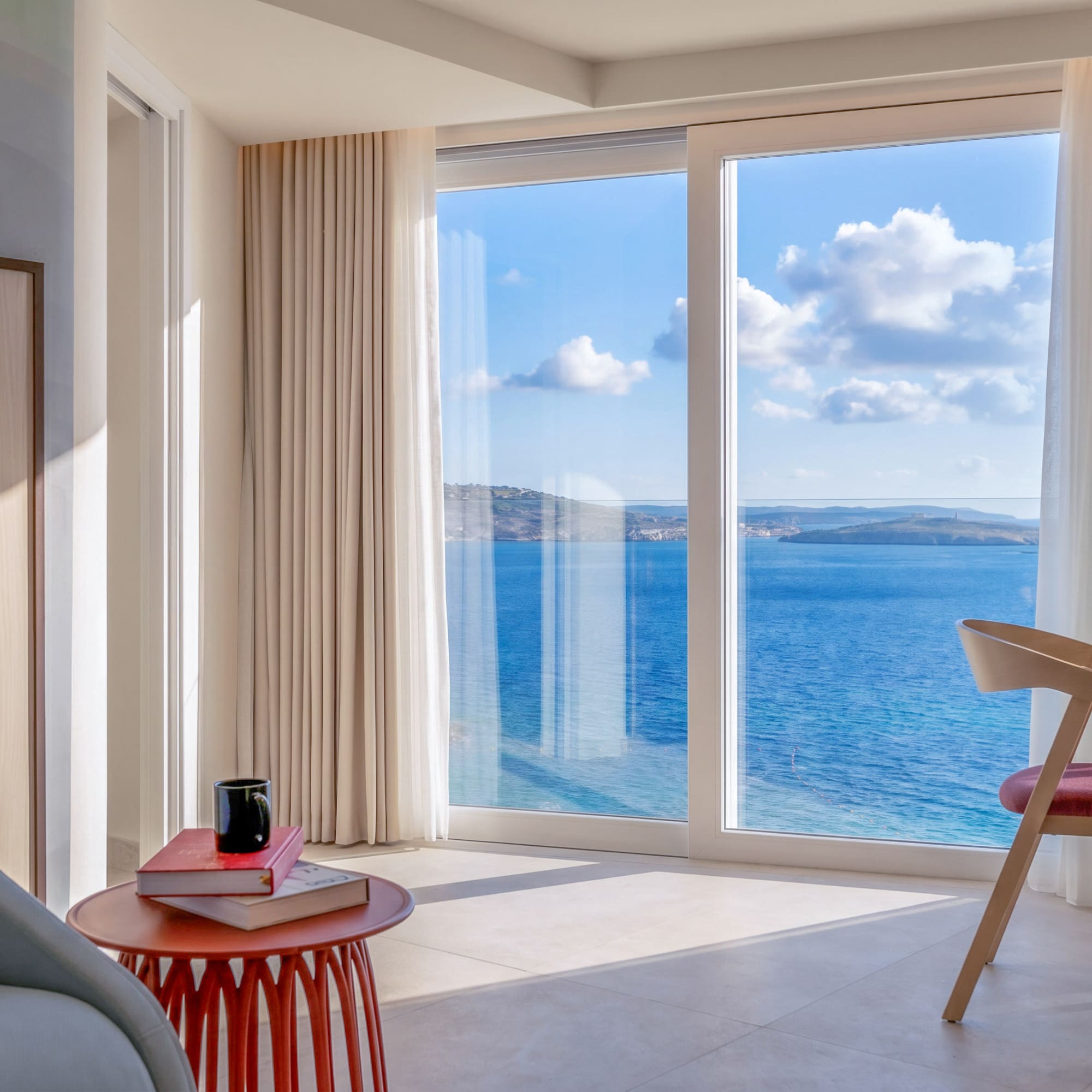 Bright modern hotel room with panoramic sea view from large window.