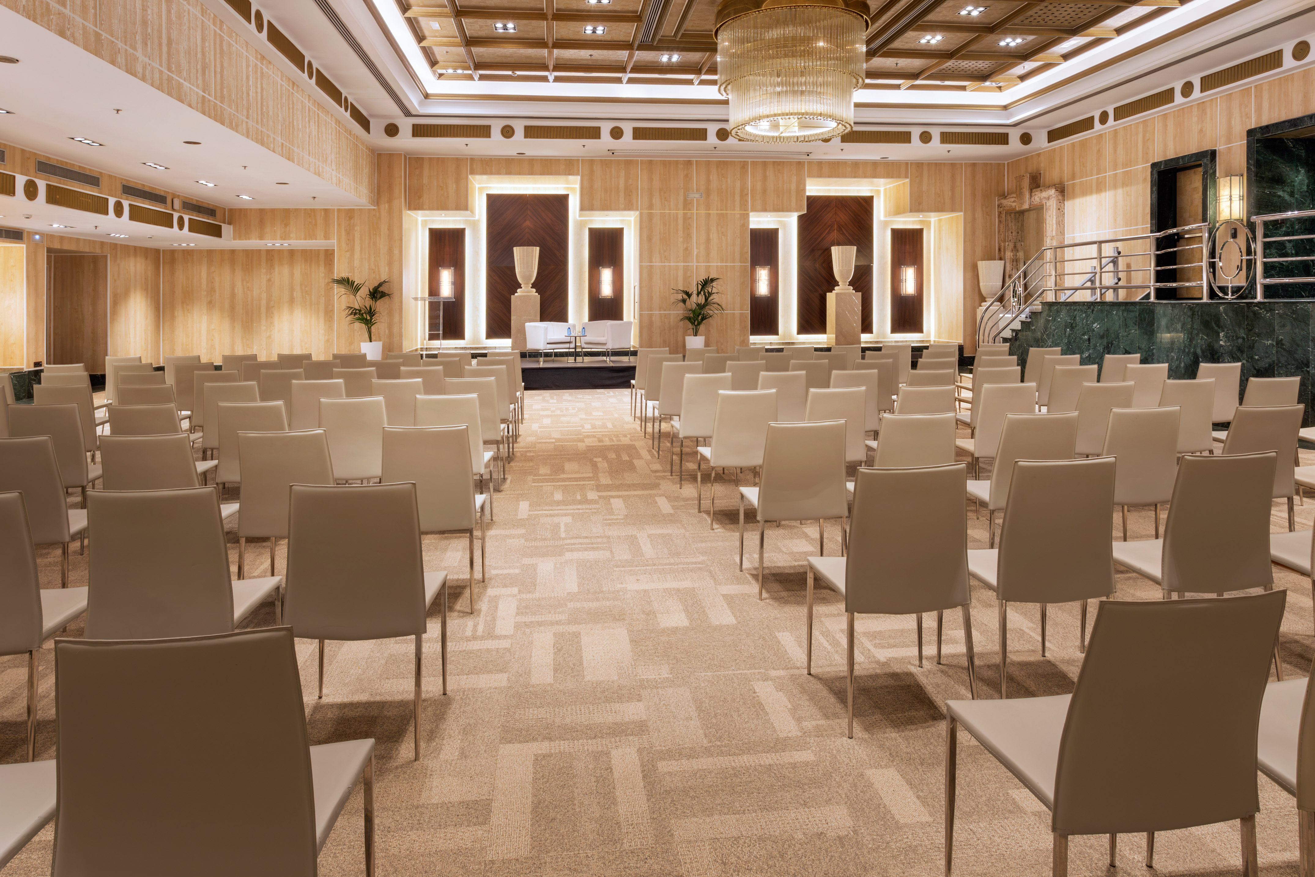 Luxury conference room, empty chairs, stage, wood paneling, and chandelier.