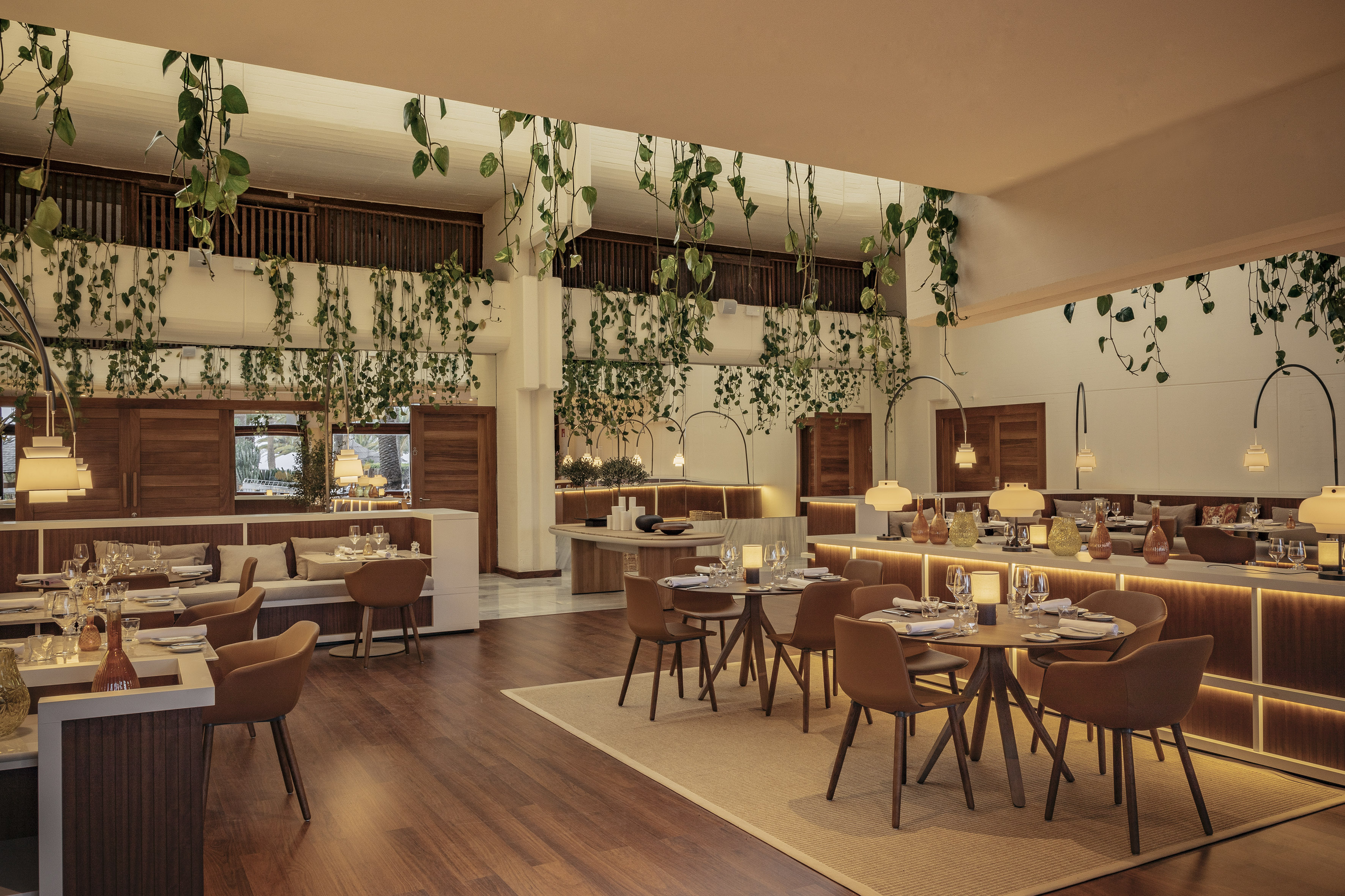 Elegant restaurant dining room with hanging greenery, wood accents, and warm lighting.