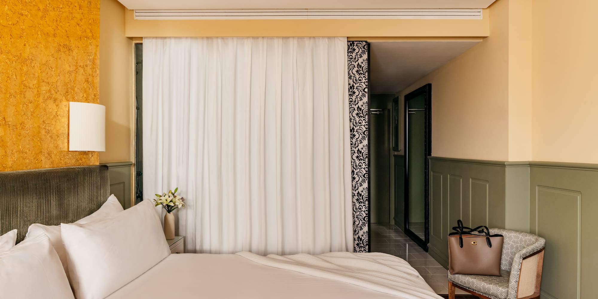 Habitación de hotel con cama, decoración moderna, pared dorada y verde.