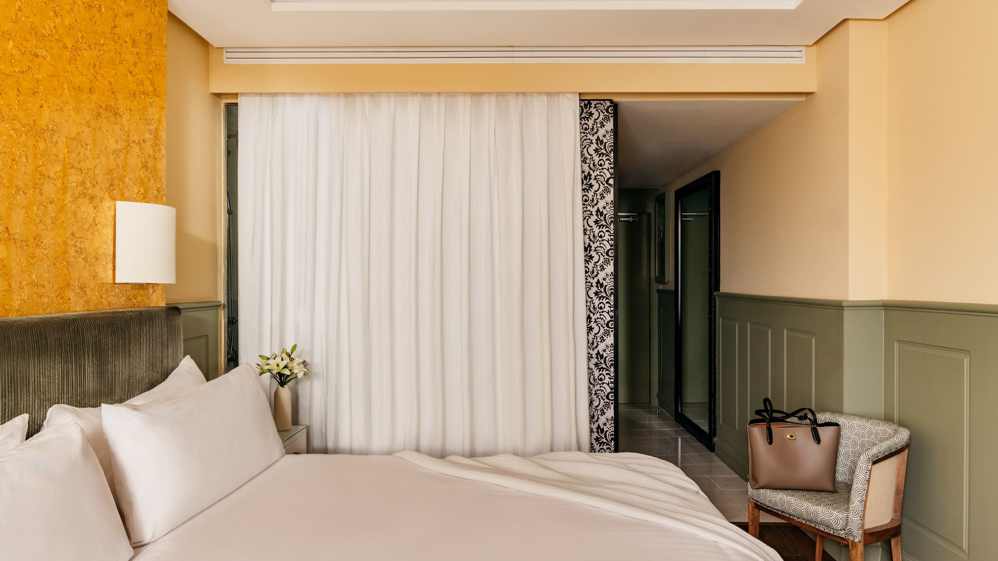 Habitación de hotel con cama, decoración moderna, pared dorada y verde.