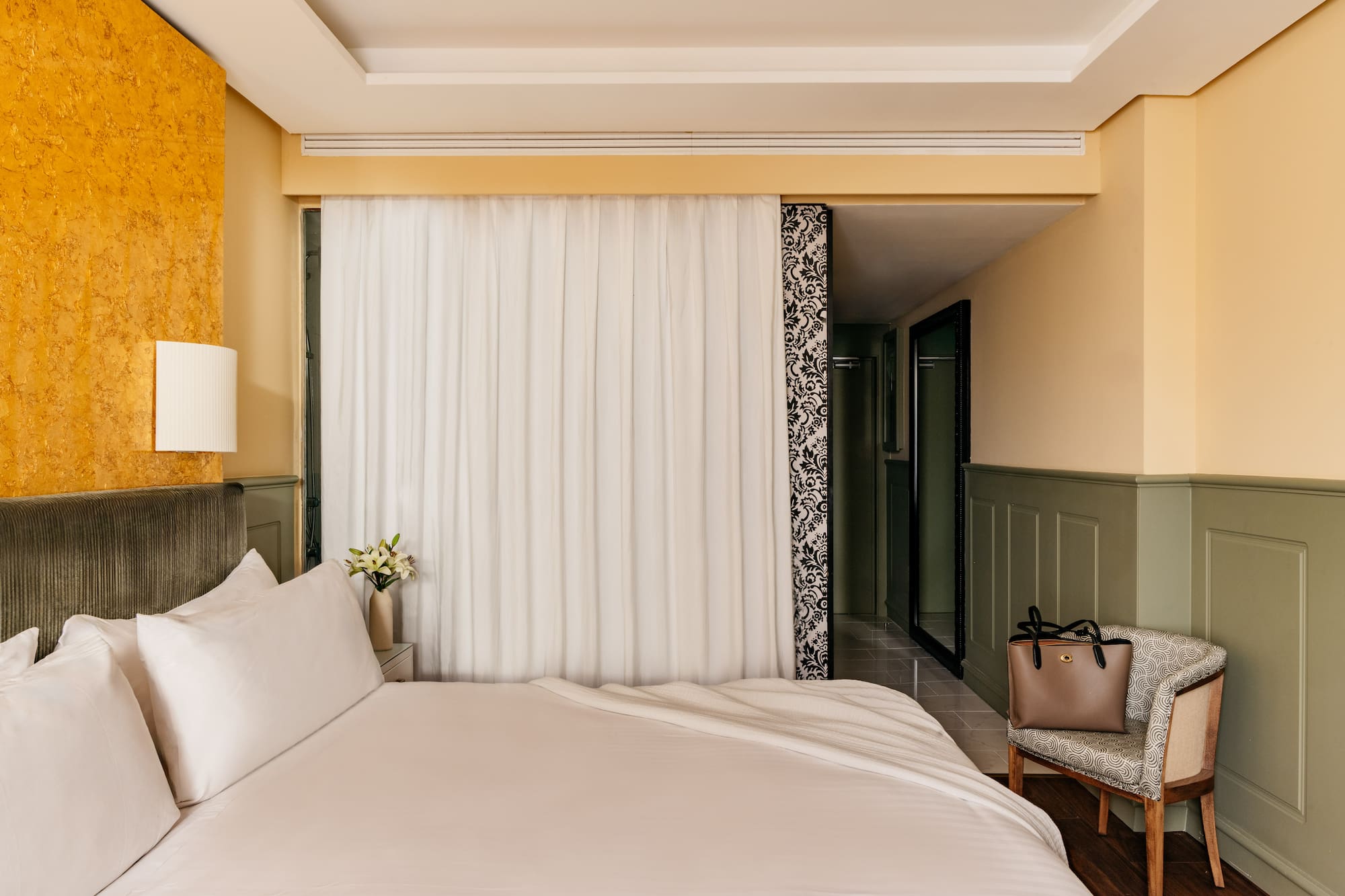 Habitación de hotel con cama, decoración moderna, pared dorada y verde.