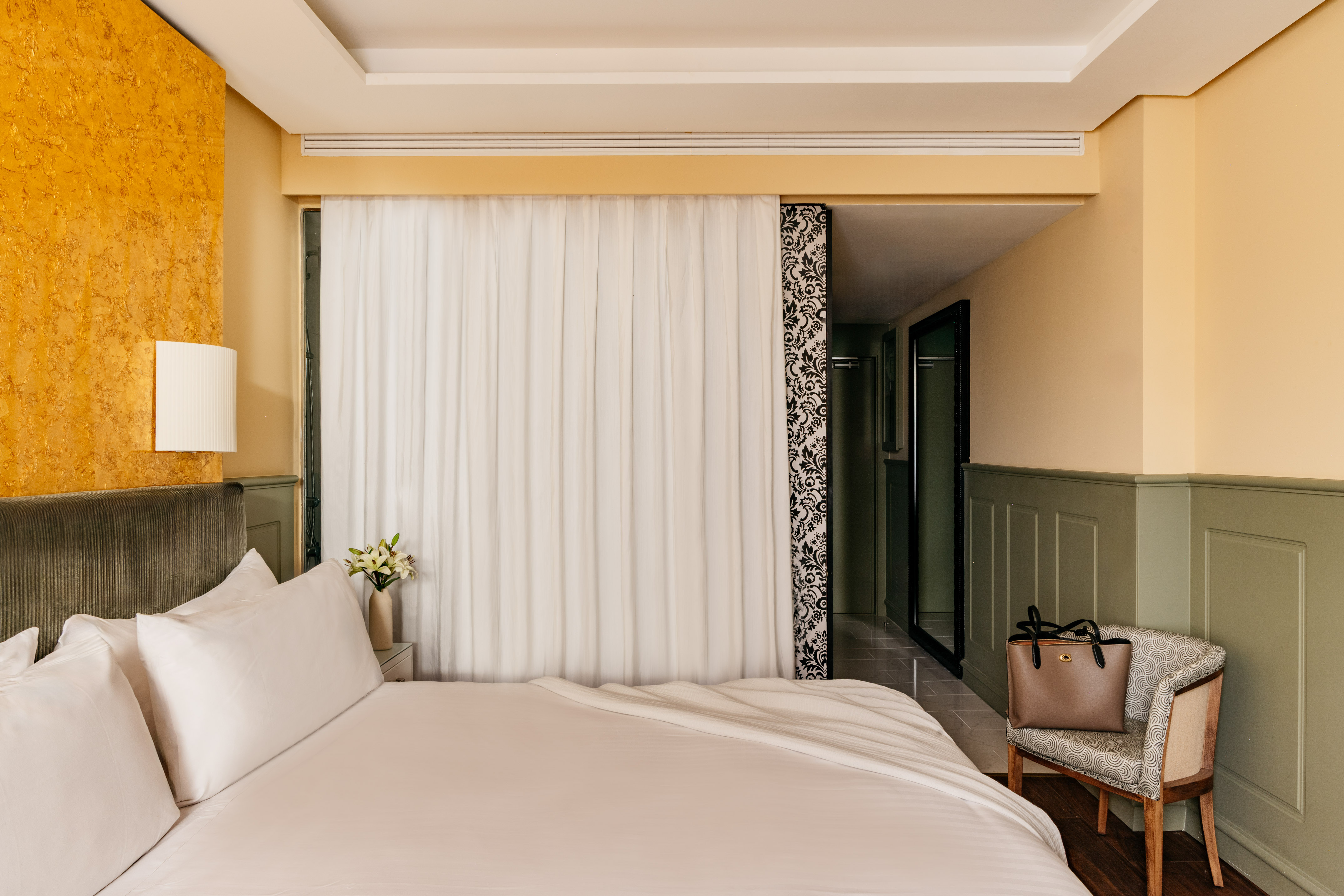 Habitación de hotel con cama, decoración moderna, pared dorada y verde.