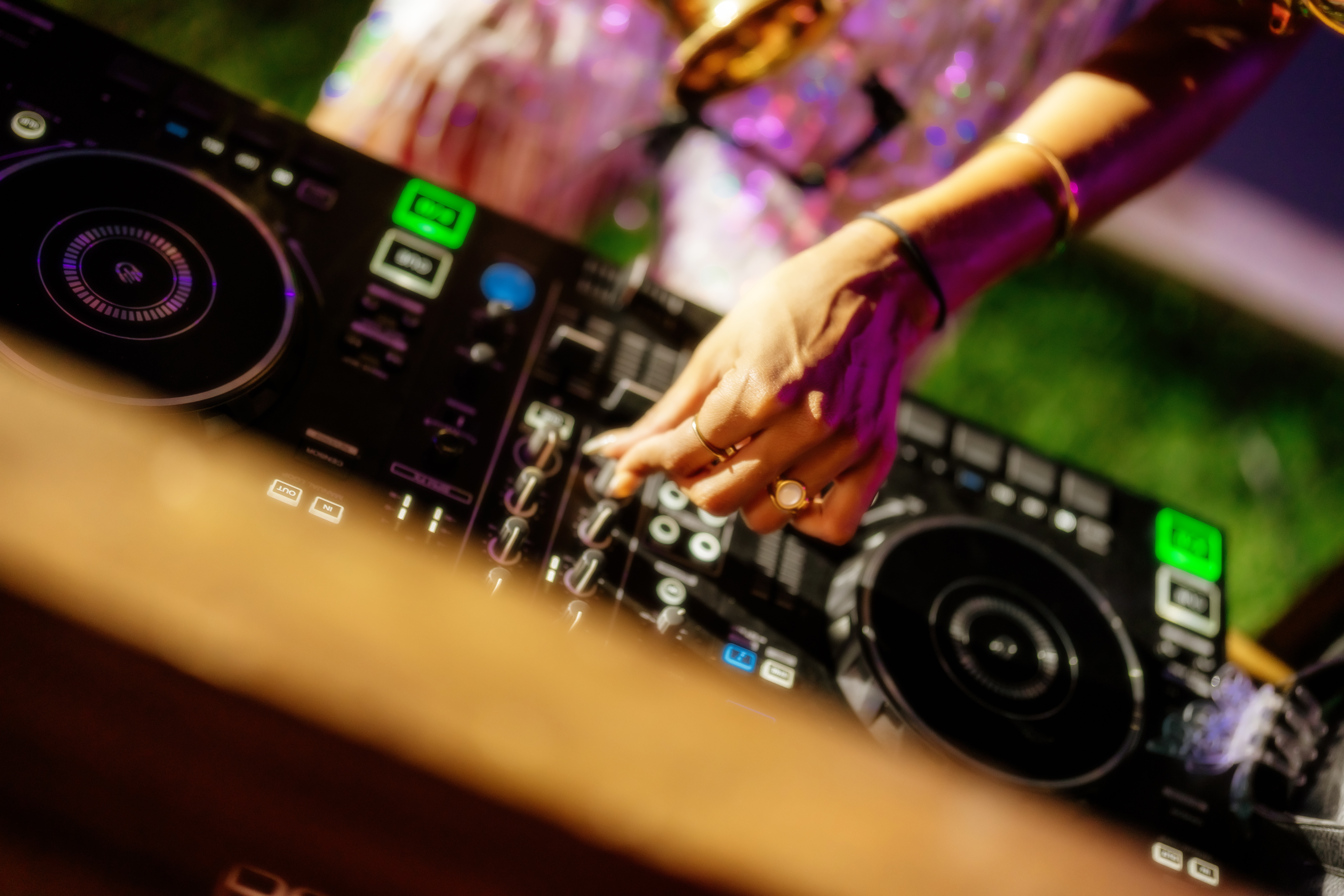 DJ's hand on mixing console, adjusting controls with glowing lights.