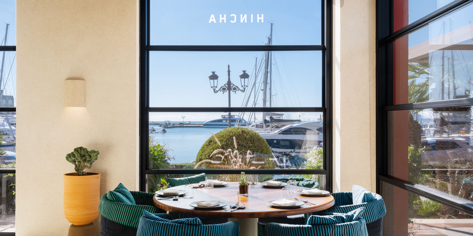 a table with plates and chairs in a room with a view of a boat and water