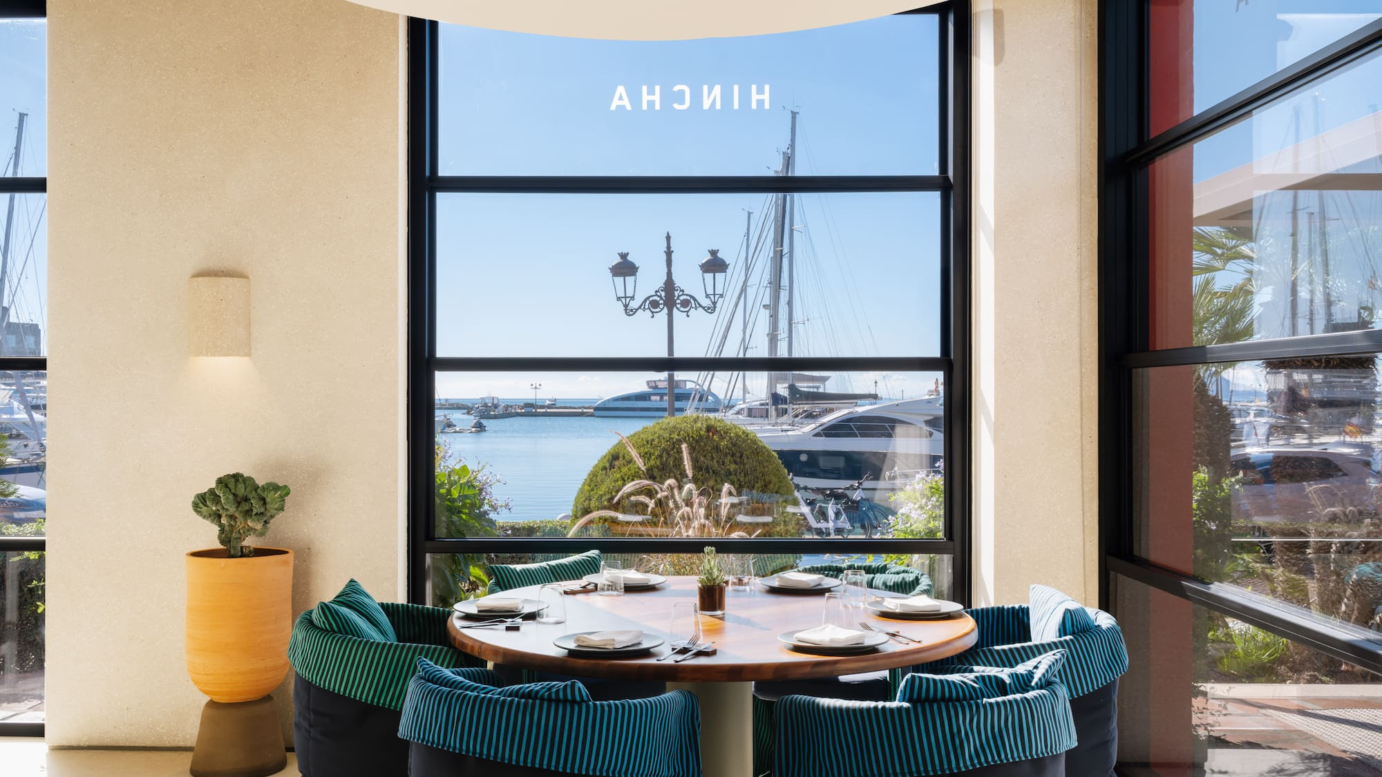 a table with plates and chairs in a room with a view of a boat and water
