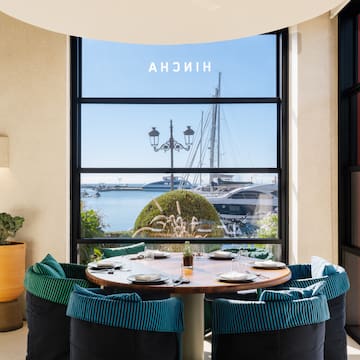 a table with plates and chairs in a room with a view of a boat and water